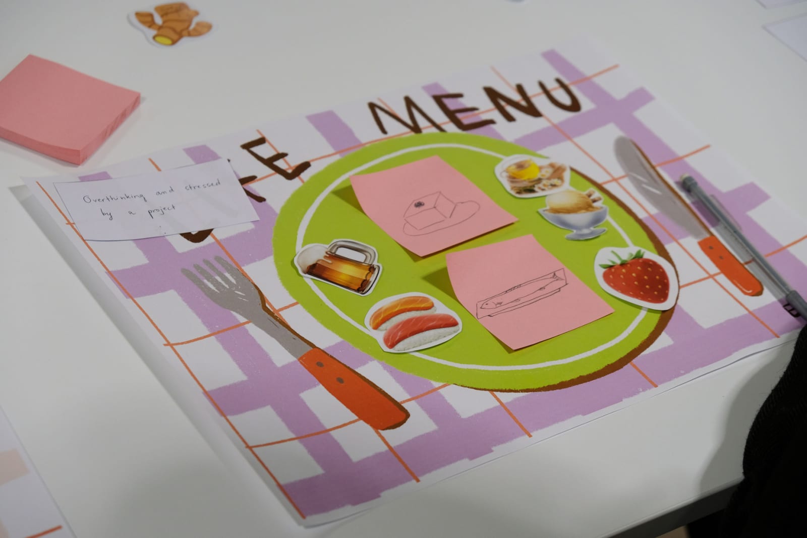 On a purple paper blanket, a paper green plate is covered by paper food items, based on emojis and sticky-notes with drawings.