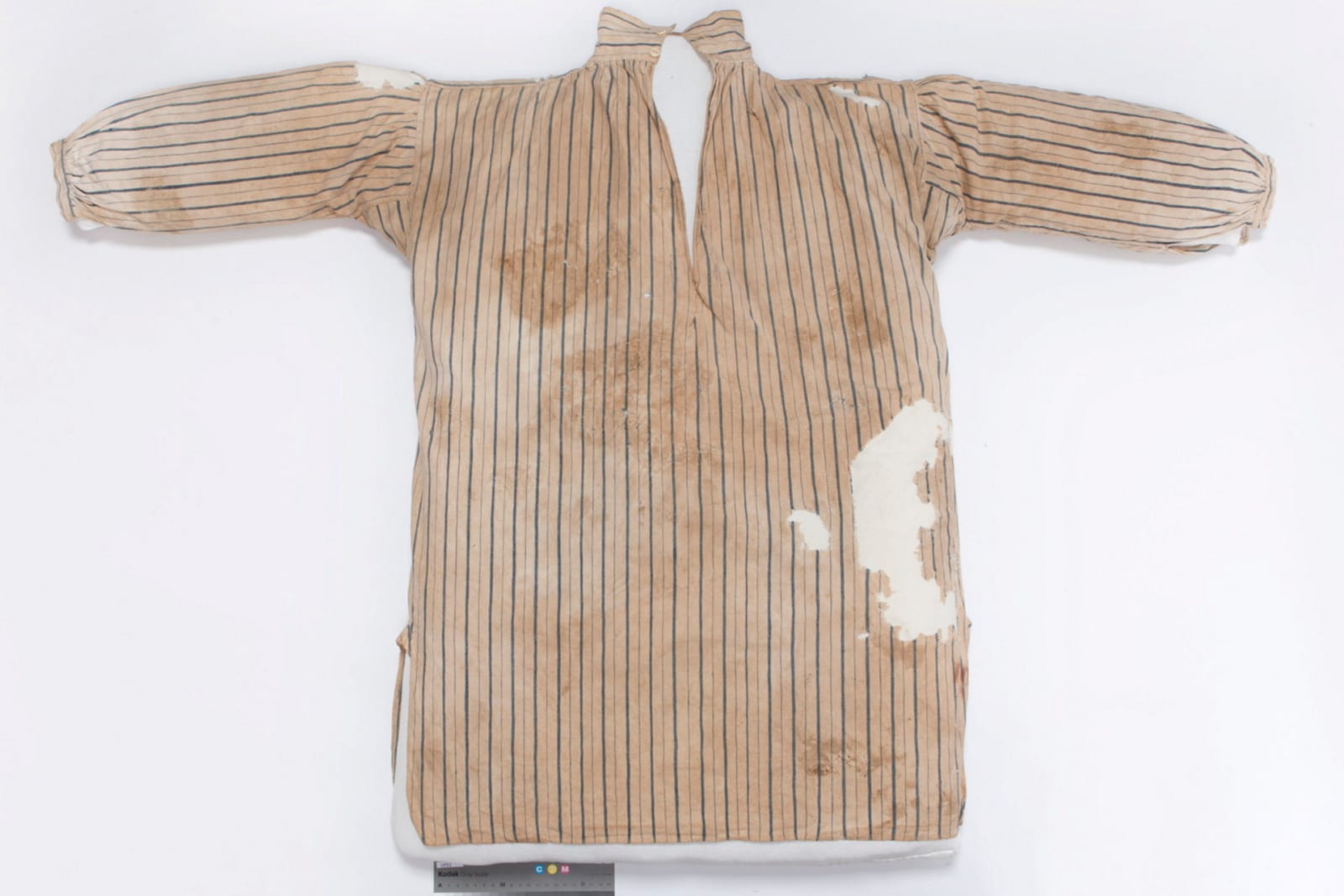A white cotton shirt with blue stripes. The shirt is stained and has many holes. A red stamp is on the lower right side. 