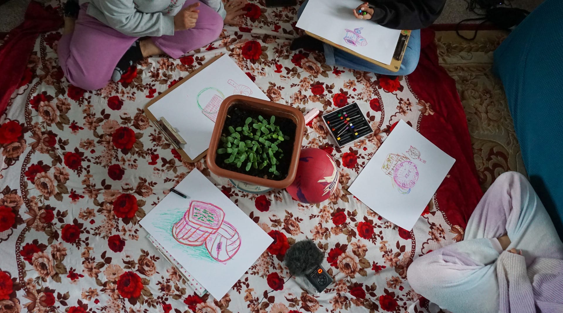 Birds eye view of oil pastel drawing with four total participants and objects in the middle surrounded by A3 drawings