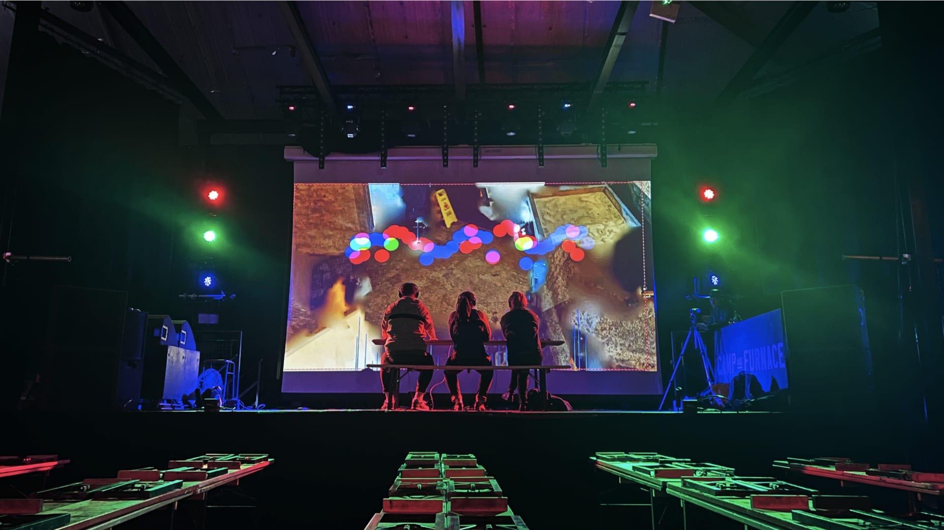 A large screen with three participants facing towards it. Red, Green and Blue marks make shapes across the screen