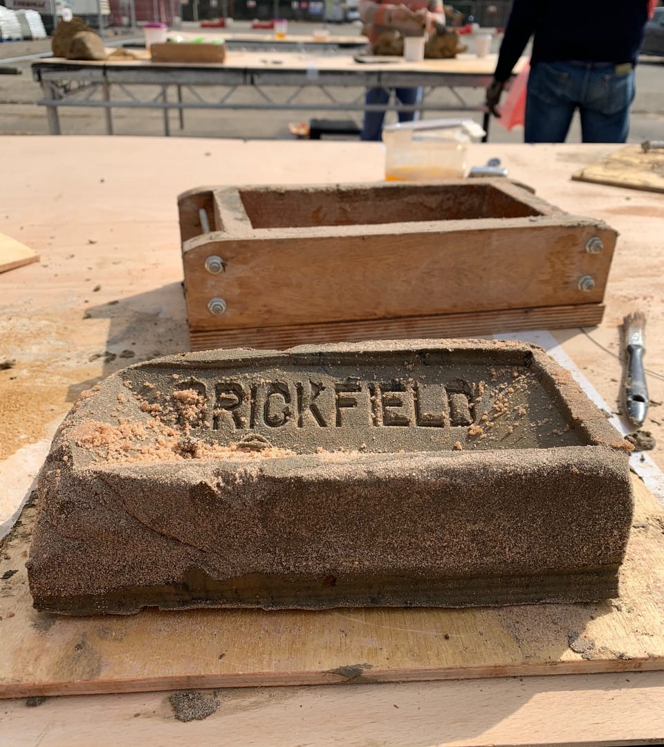 Handmade brick and wooden mould, on table, with two brickmakers around a table in background