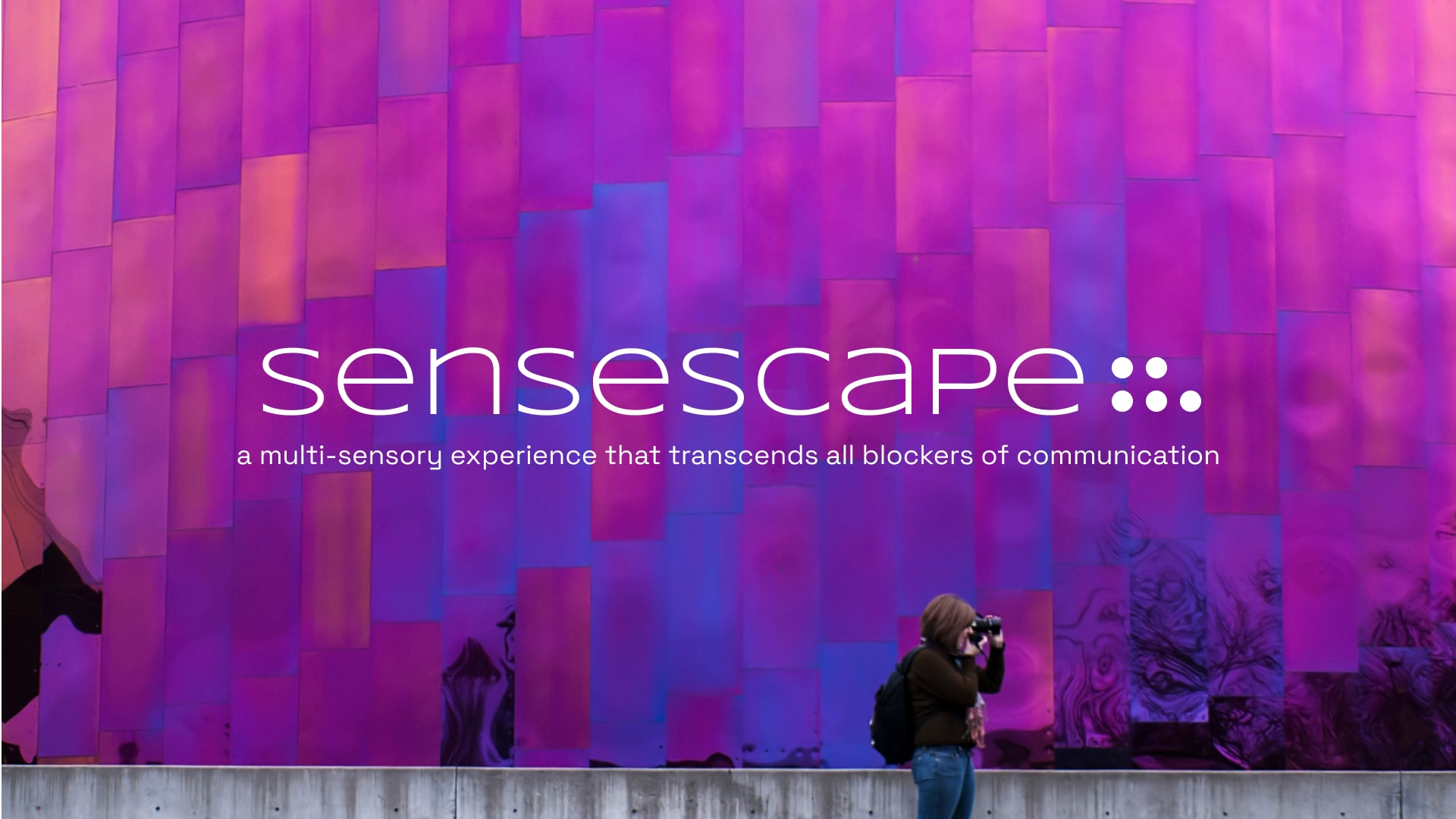 A person on the right captures a photo of a vibrant, purple-coloured wall.