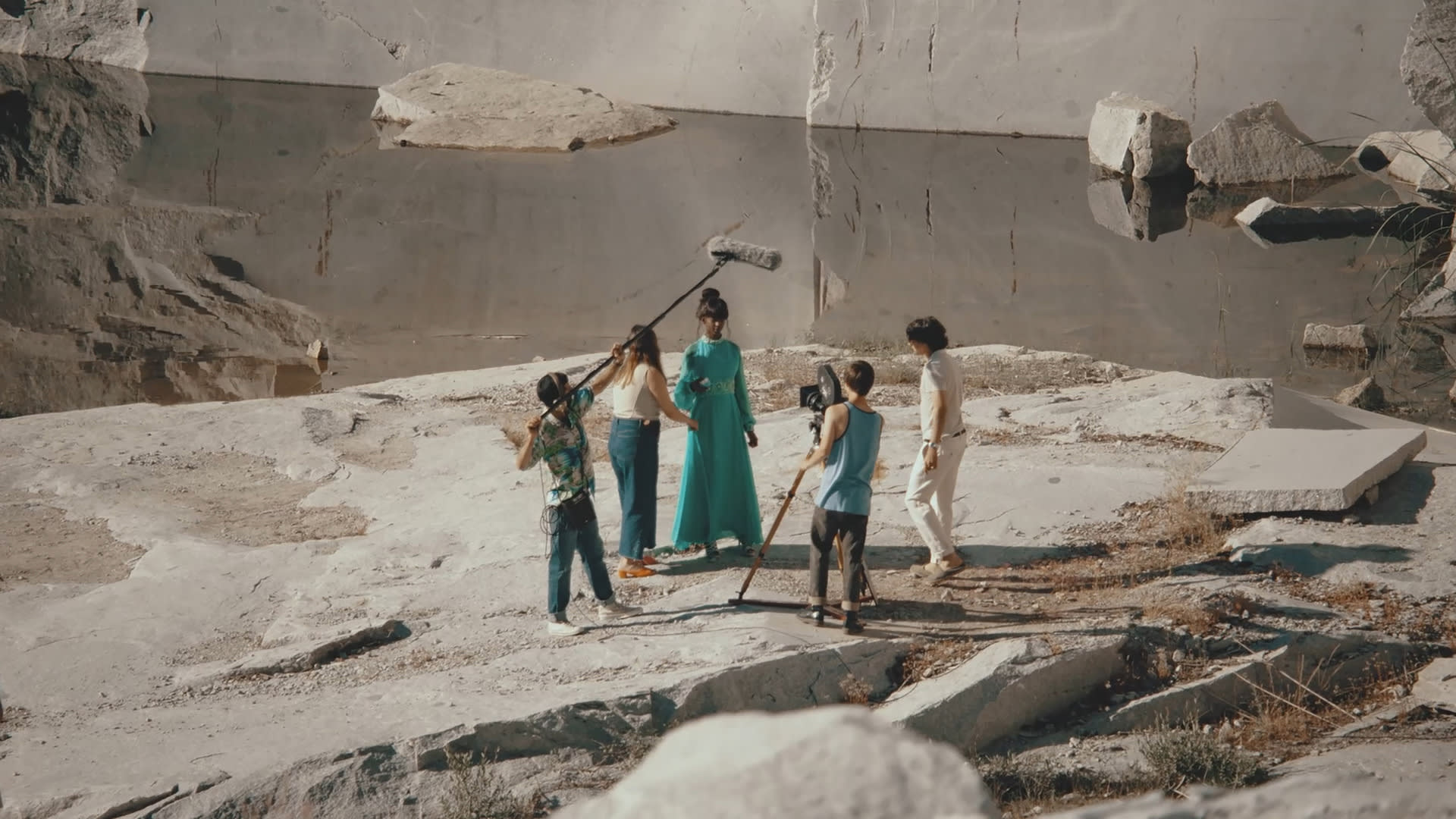 Actress with a long aqua dress, surrounded by four people assisting in an outdoor film shoot, based in a Spanish stone quarry 