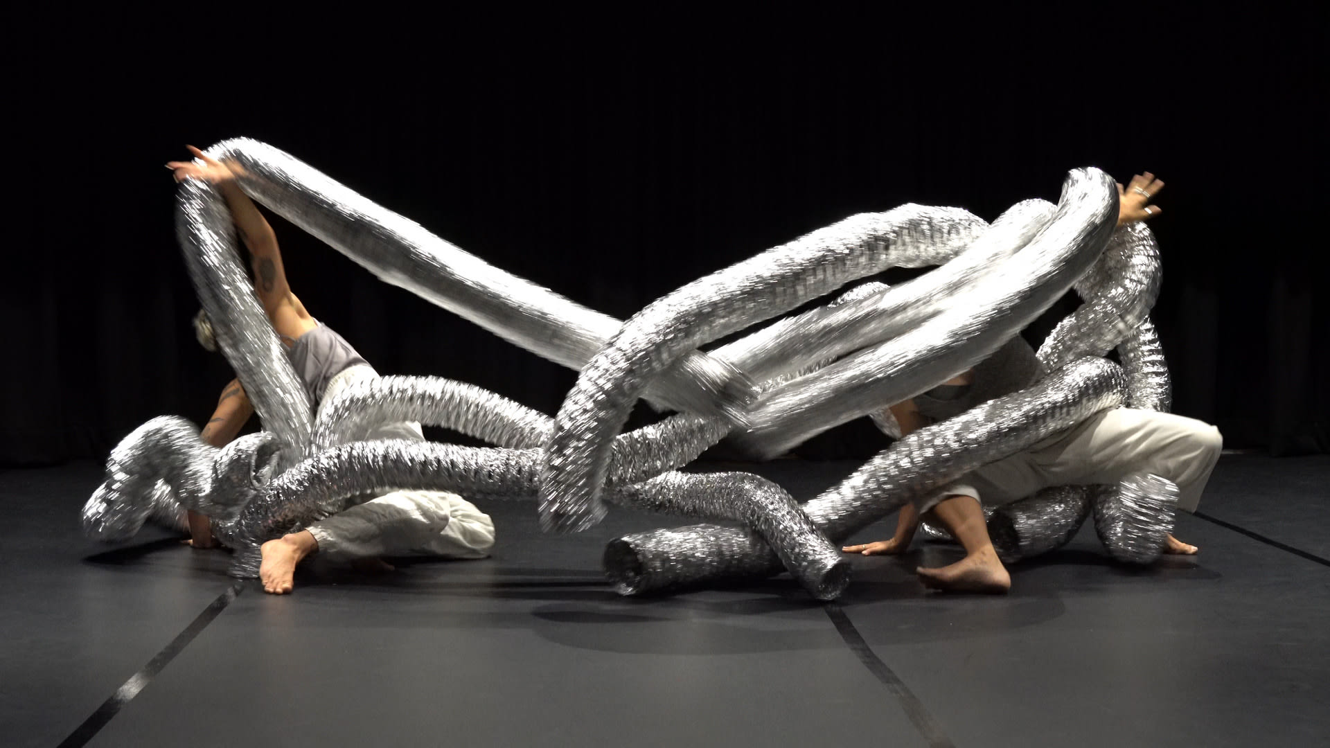 Creative development image of SUB, feature dancers entangled in silver pipes.