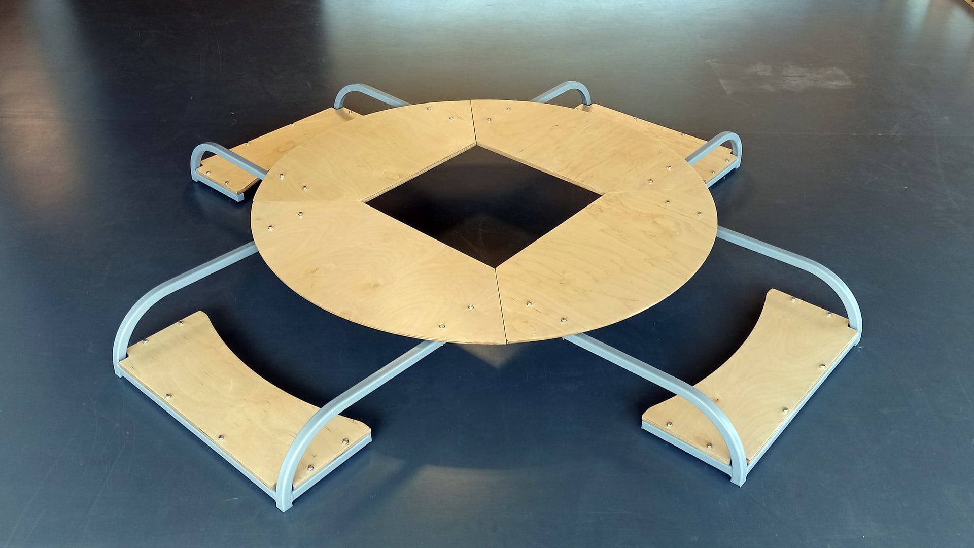 4 equidistant seats around a circular table with a square hole in the middle. All made in birch plywood. All the elements are connected by a satin grey metal structure. neither the table nor the seats