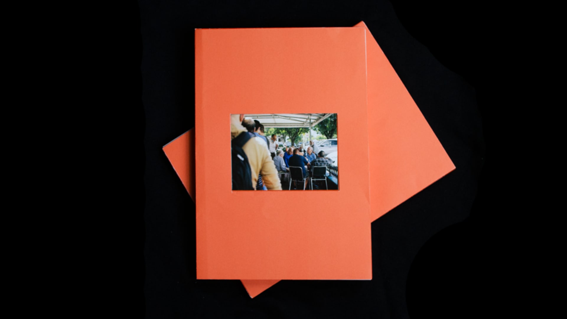 Two orange books on top of each other. The to one has a cut out window revealing a photograph of a group at a ventanita. 