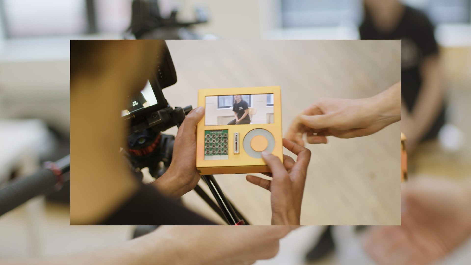 "Mix Clip", a portable video editing device, with a screen, a touch wheel, and some buttons, being handed to a camera operator.