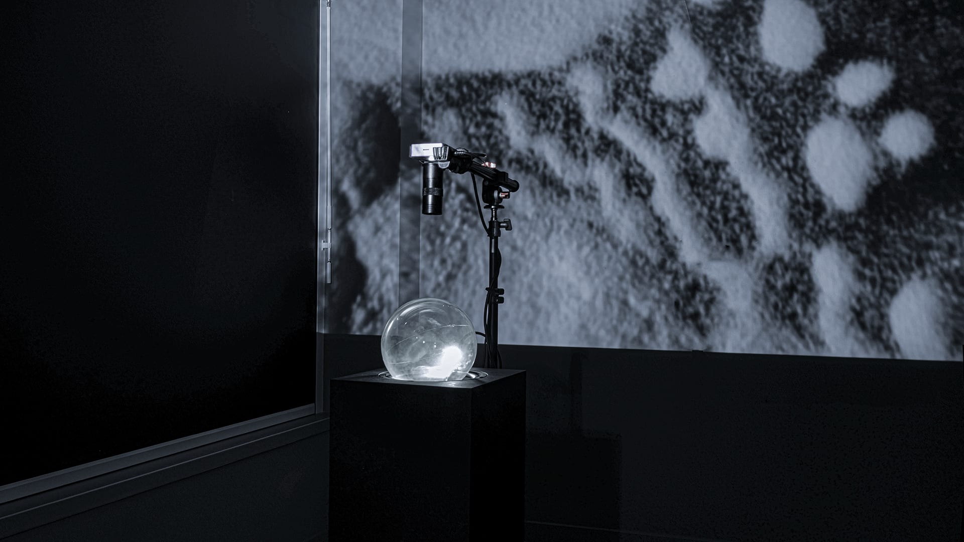 The photo depicts an art installation composed of a black box, a balloon, a camera, and a projection