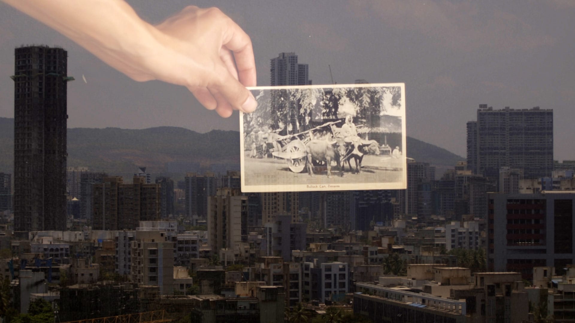 View of industrial centres and high rise buildings in Mumbai, India, hand holding old postcard superimposed. 