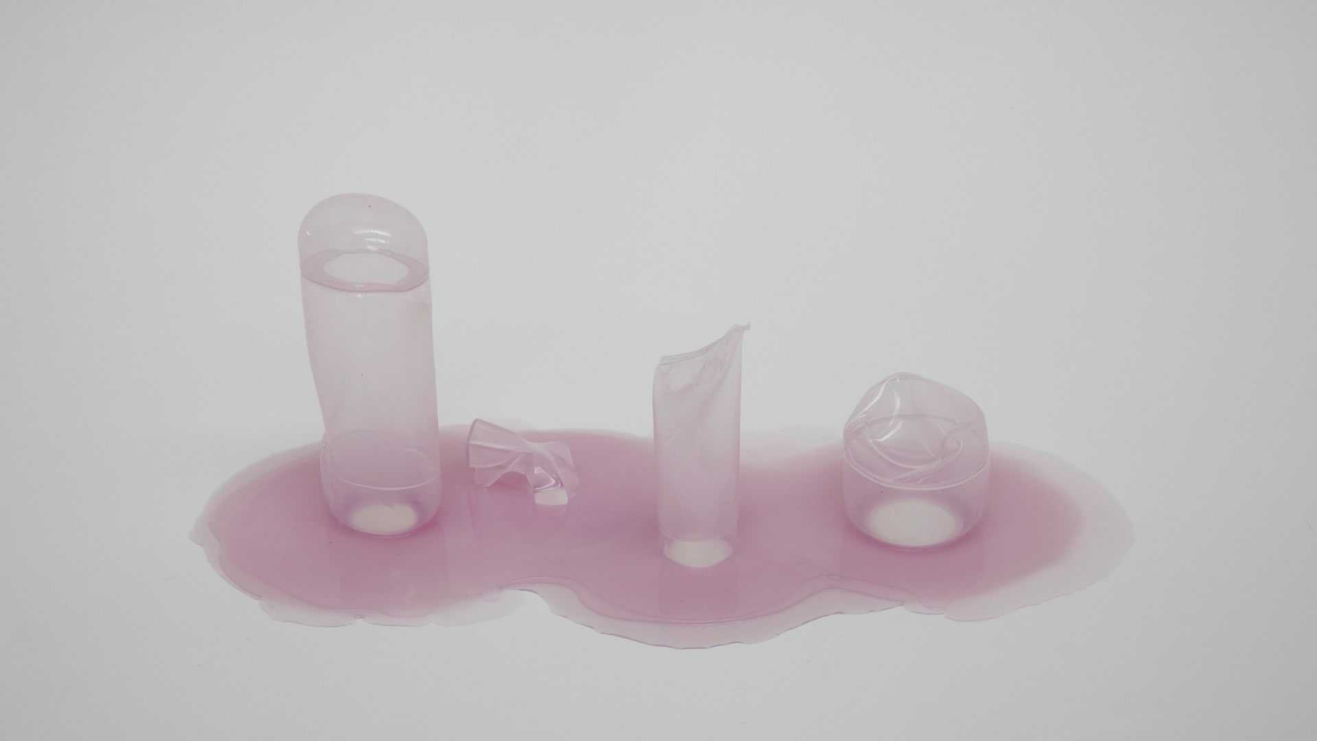 Row of 4 cosmetic bottles in thin translucent silicone skin casts. In purple.