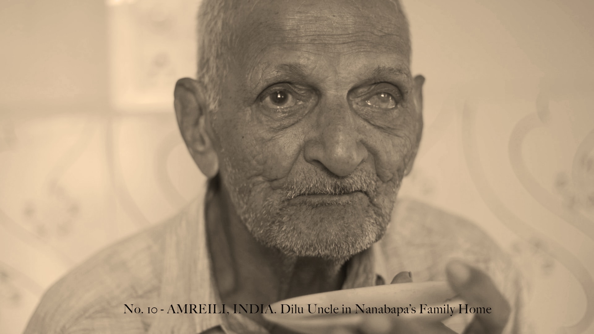 sepia image of man drinking tea in his home in Amreili, Gujarat, India with caption "No. 10 - AMREILI, INDIA"