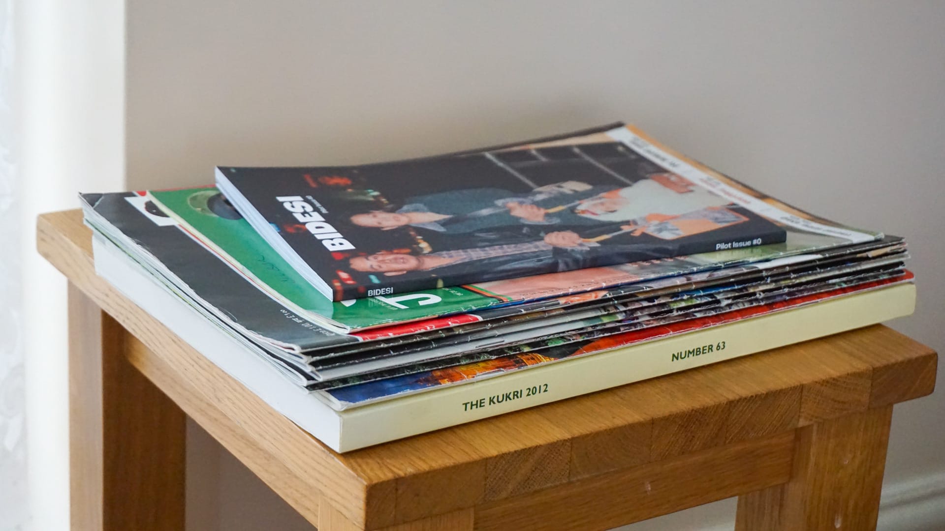 Bidesi zine placed on top of a stack of Ashmina's late grandfathers Nepali Magazine archive, on top of a wooden side table