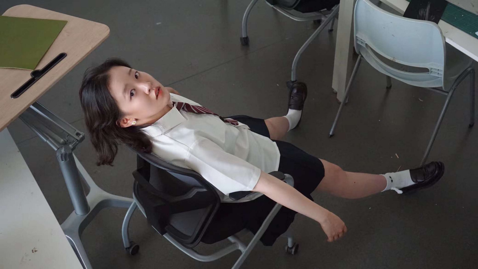 A girl sits sideways on a chair, turning her head to look at the camera.