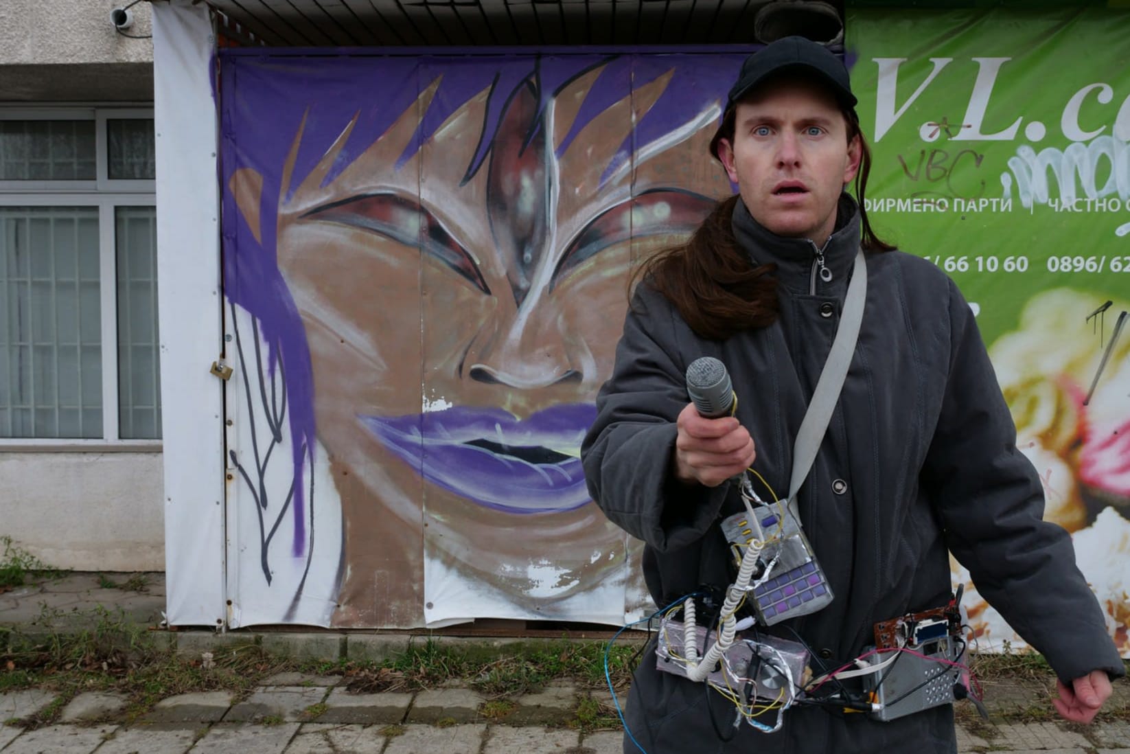 man sanding in front of a shop holding a homemade device similar to a metal detector