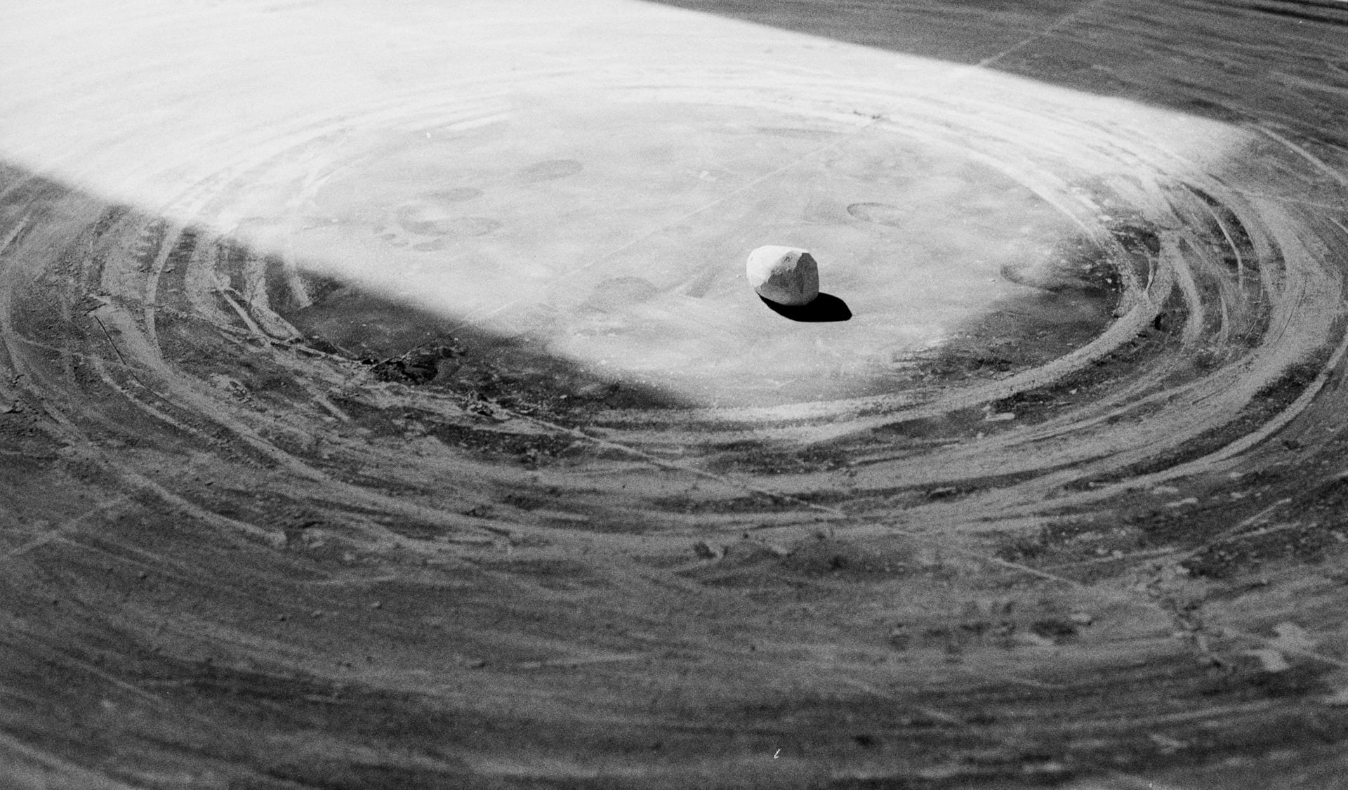  image showing a section of a circular drawing made with chalk on a black board. in the middle sits a lump of chalk. 