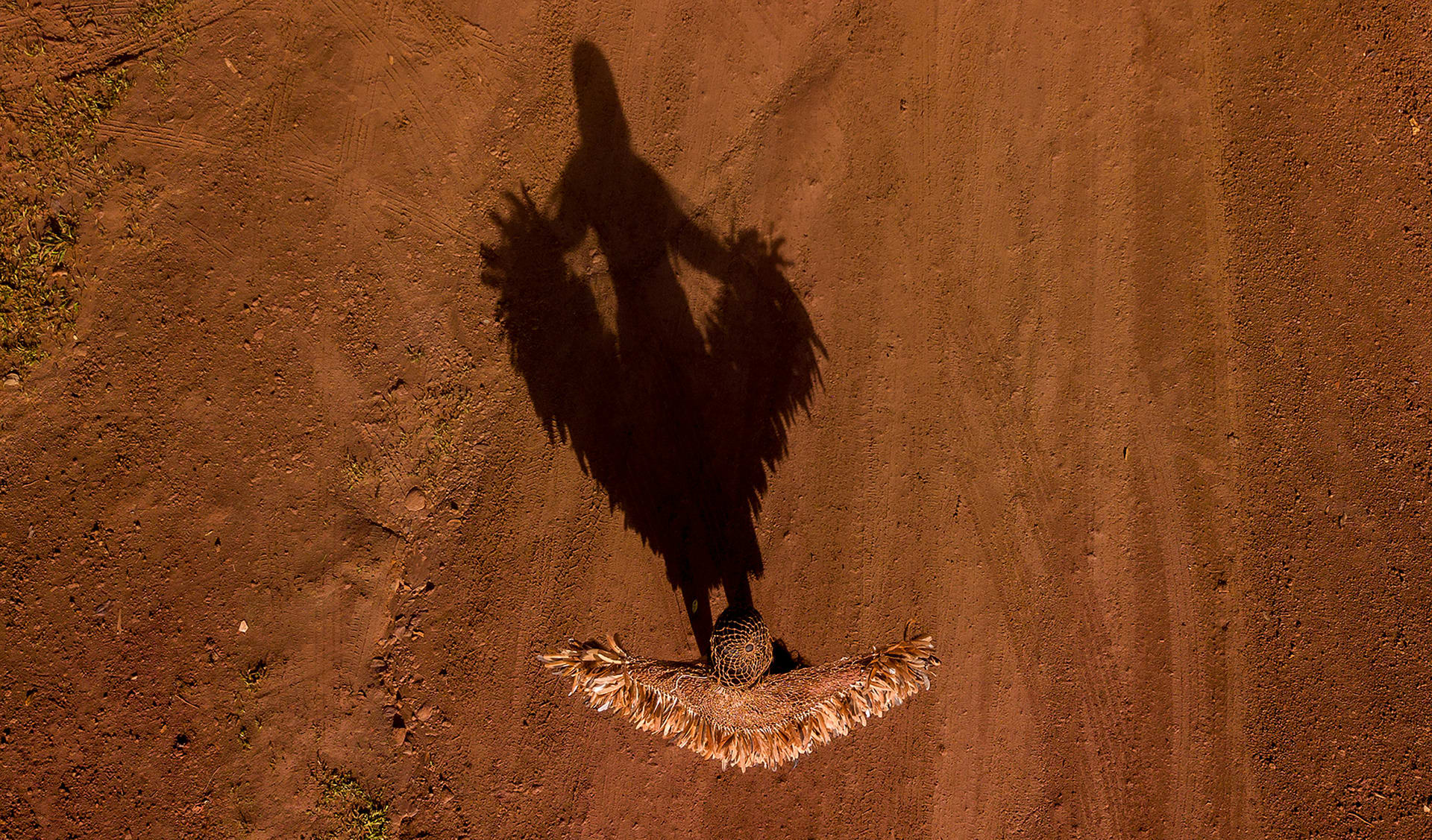 Above bird eye view of woman wearing a Tupinambá cape, make of string and feathers. You can see shadow of the female body.