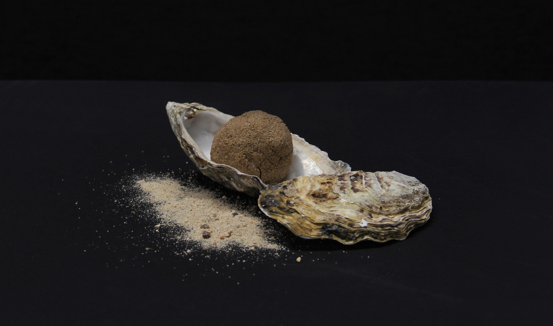 An oyster shell with imitation eggs made with sand and oyster shell on a black background with scattered sand.