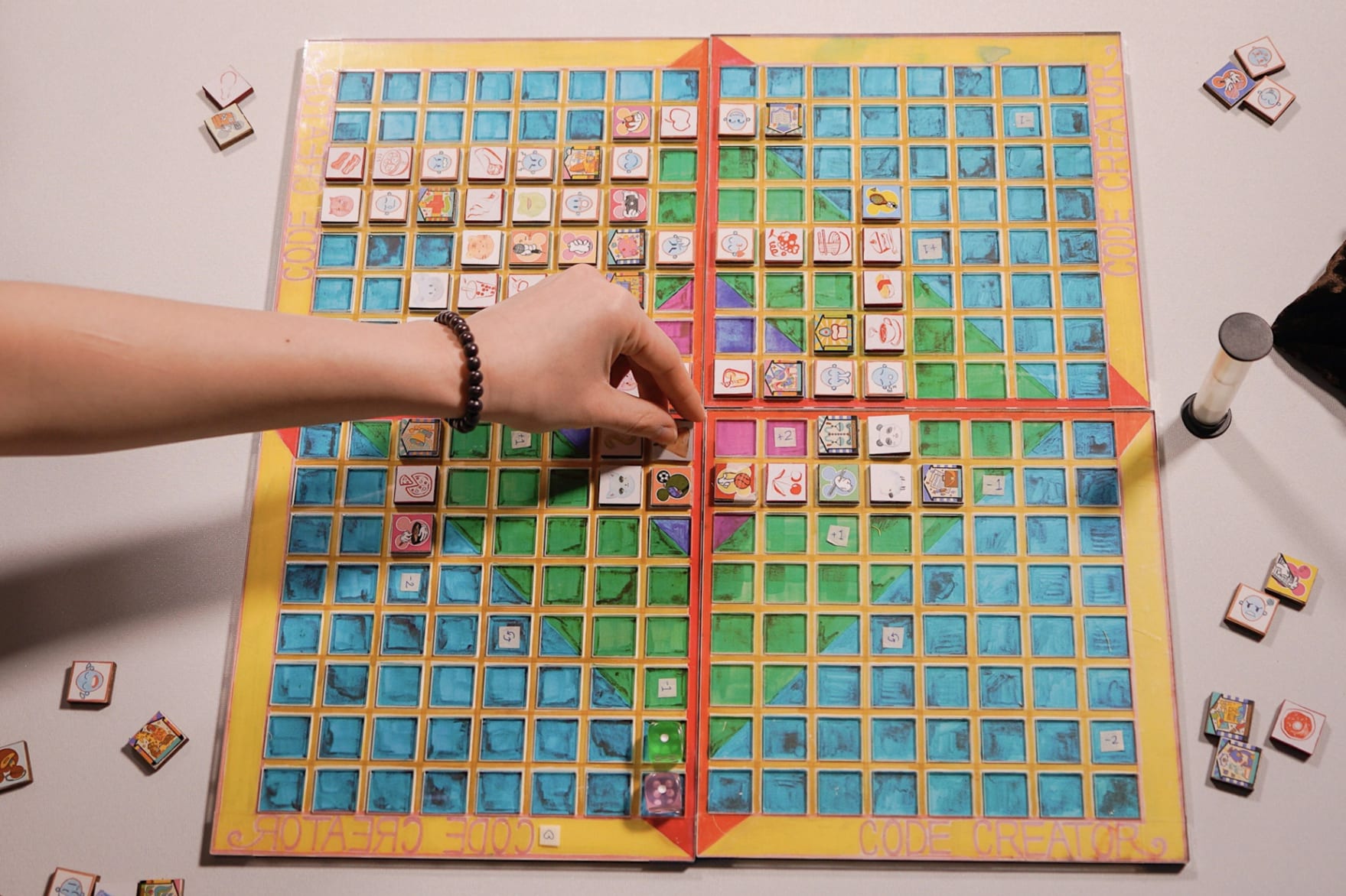 Board game shown with square tiles. A player's hand is placing the code tile (animal category) to complete a sentence on board.