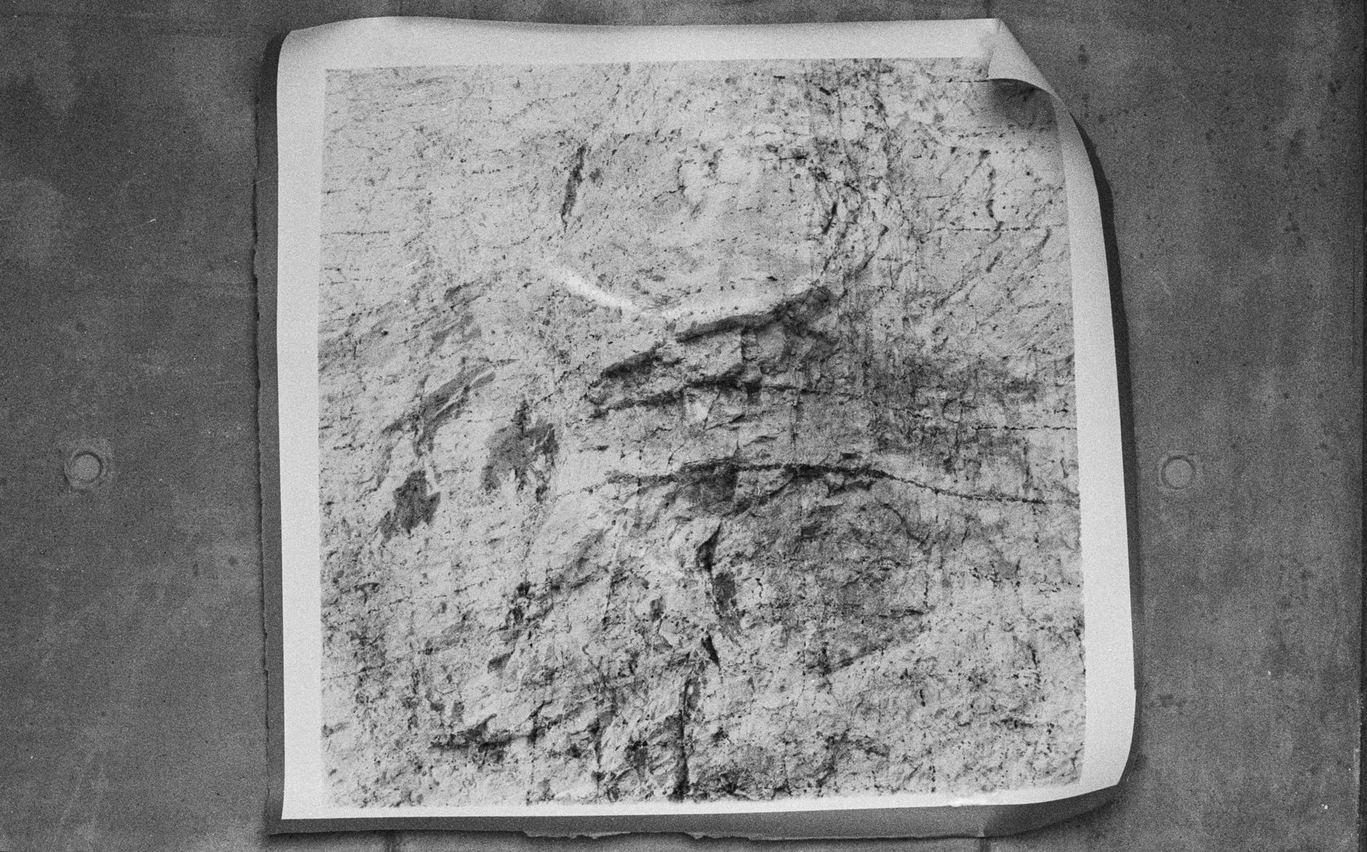 Image of a large darkroom print hanging on a stone wall. The Print is of a chalk cliff face. 