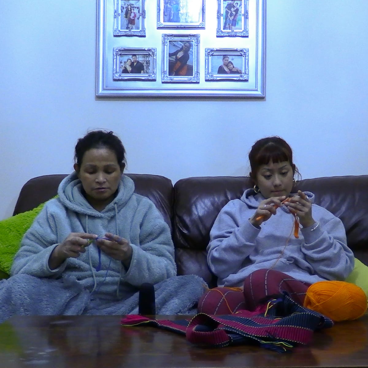 Ashmina and her mother crocheting individually sat on a brown leather sofa in their living room.