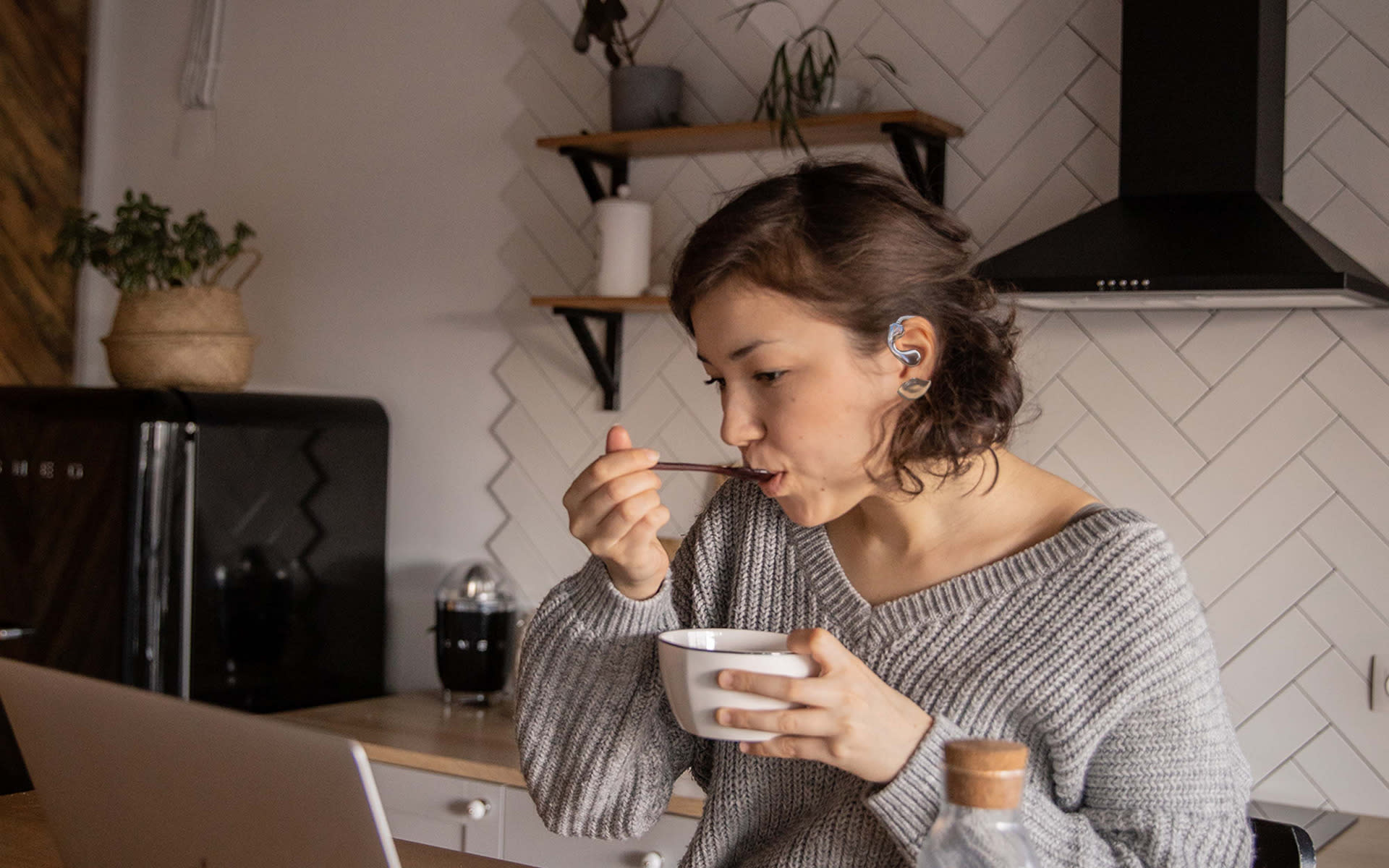 a yound lady wearing Mnemosyne, eating food and sitting in front of a laptop, looks realxing