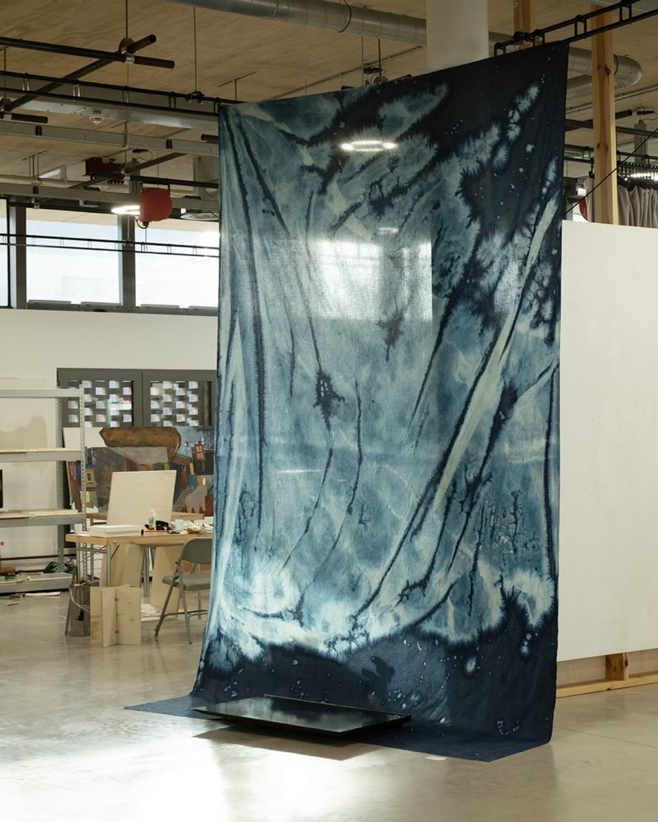 Installation shot of a large blue print hanging in studio space