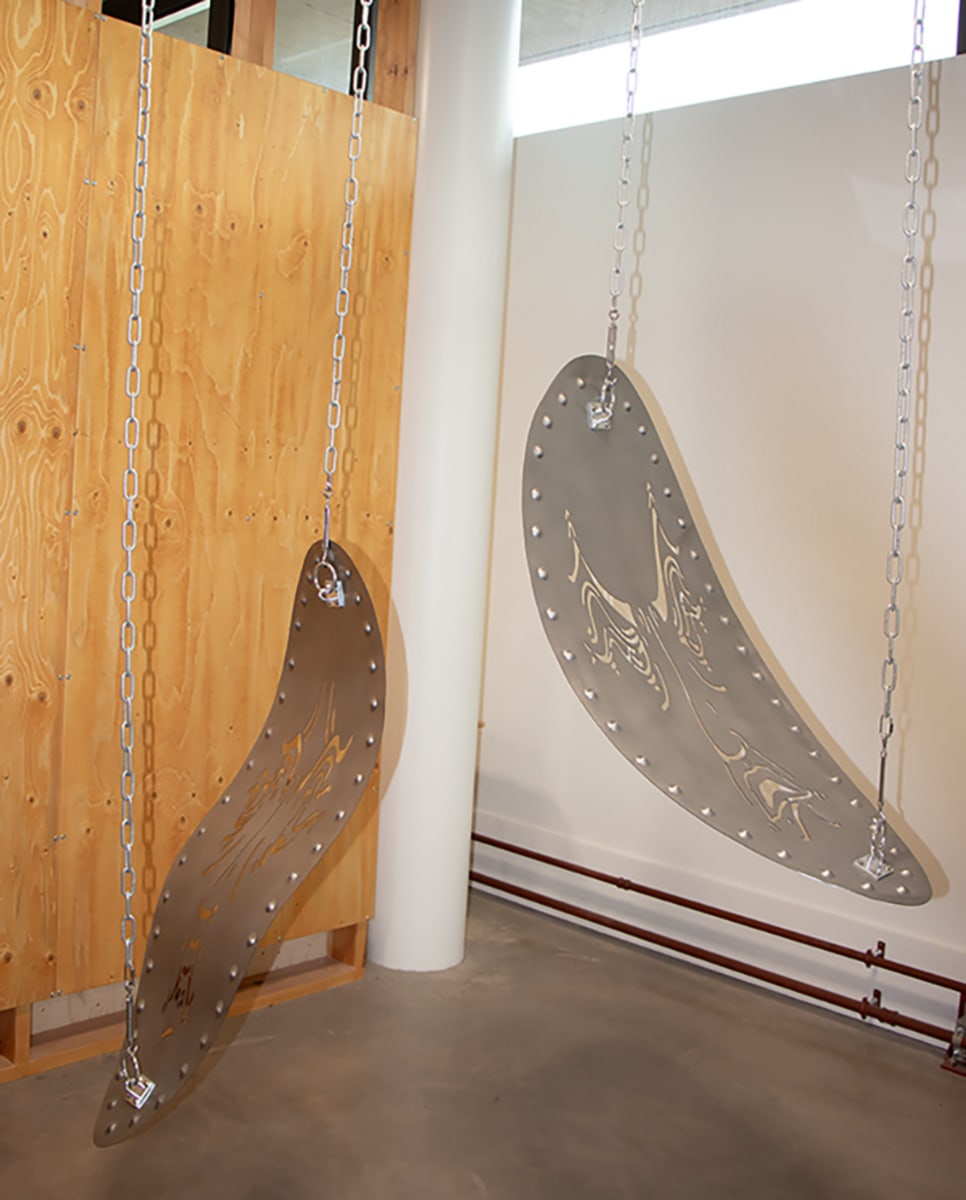 Zoom in of two hanging shields with faces cut out. Both are hung with metal chains 