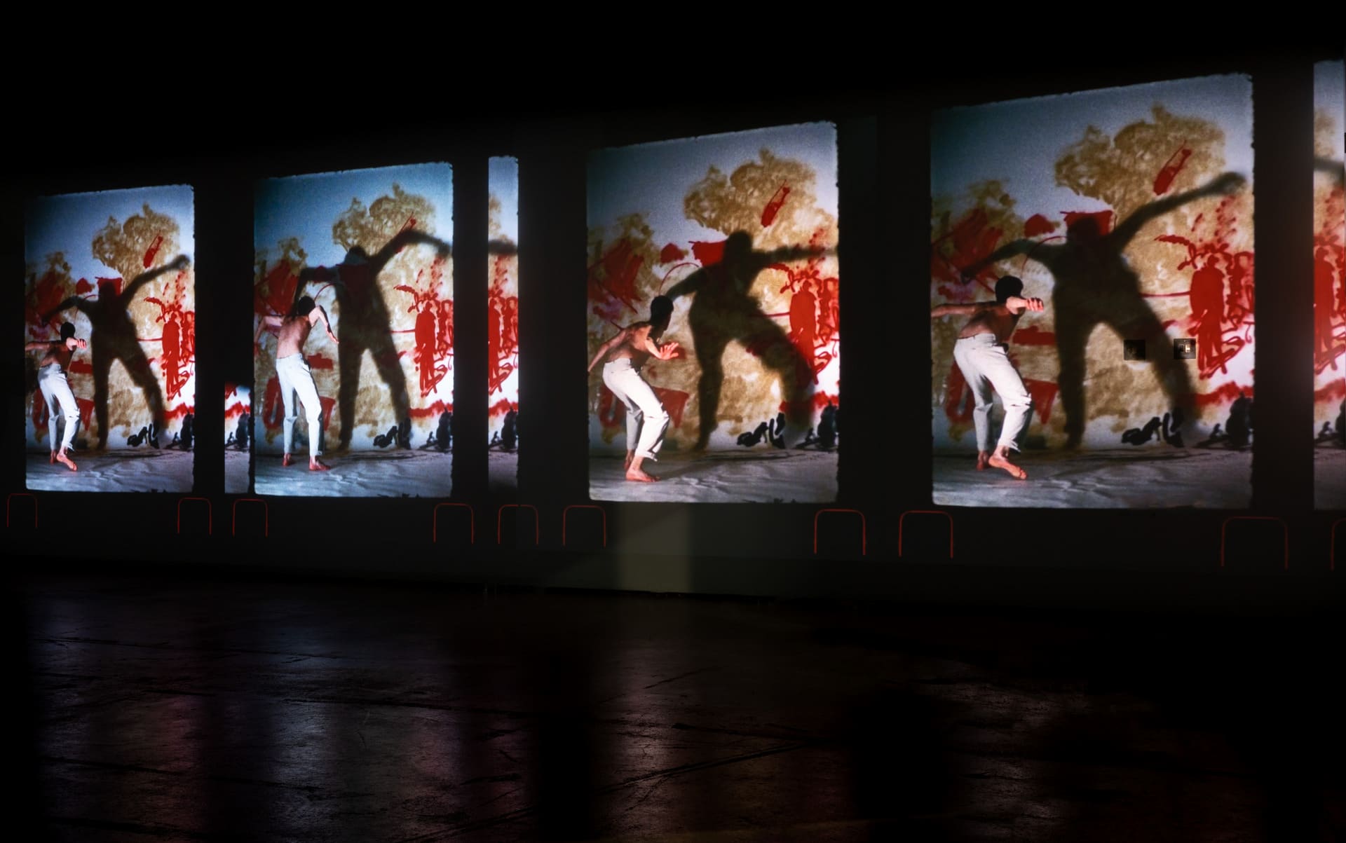 a video projection of several figures standing in front of a red painted backdrop