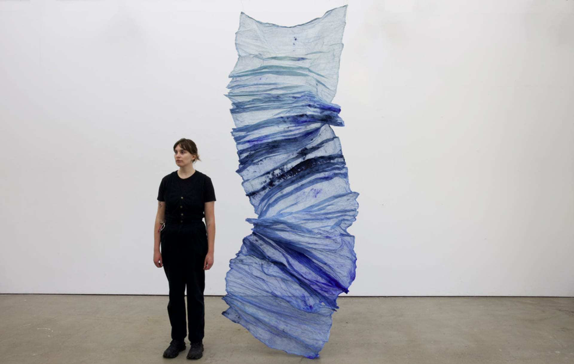 Samara standing next to her blue sculpture work titled "The Crossing"