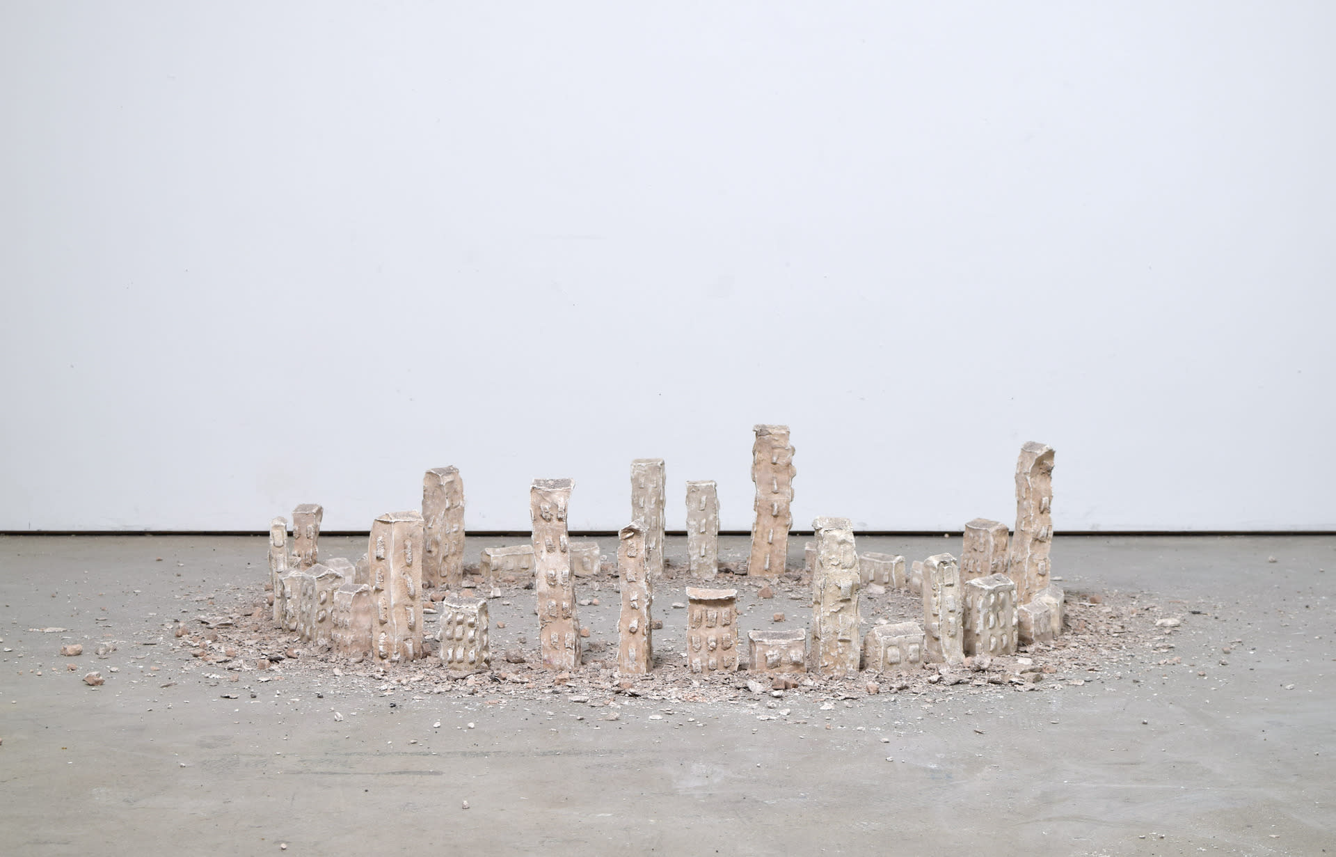 Thirty plaster towers ranging in height from 30-6cm, are positioned in a large circle on the floor with a halo of rubble.