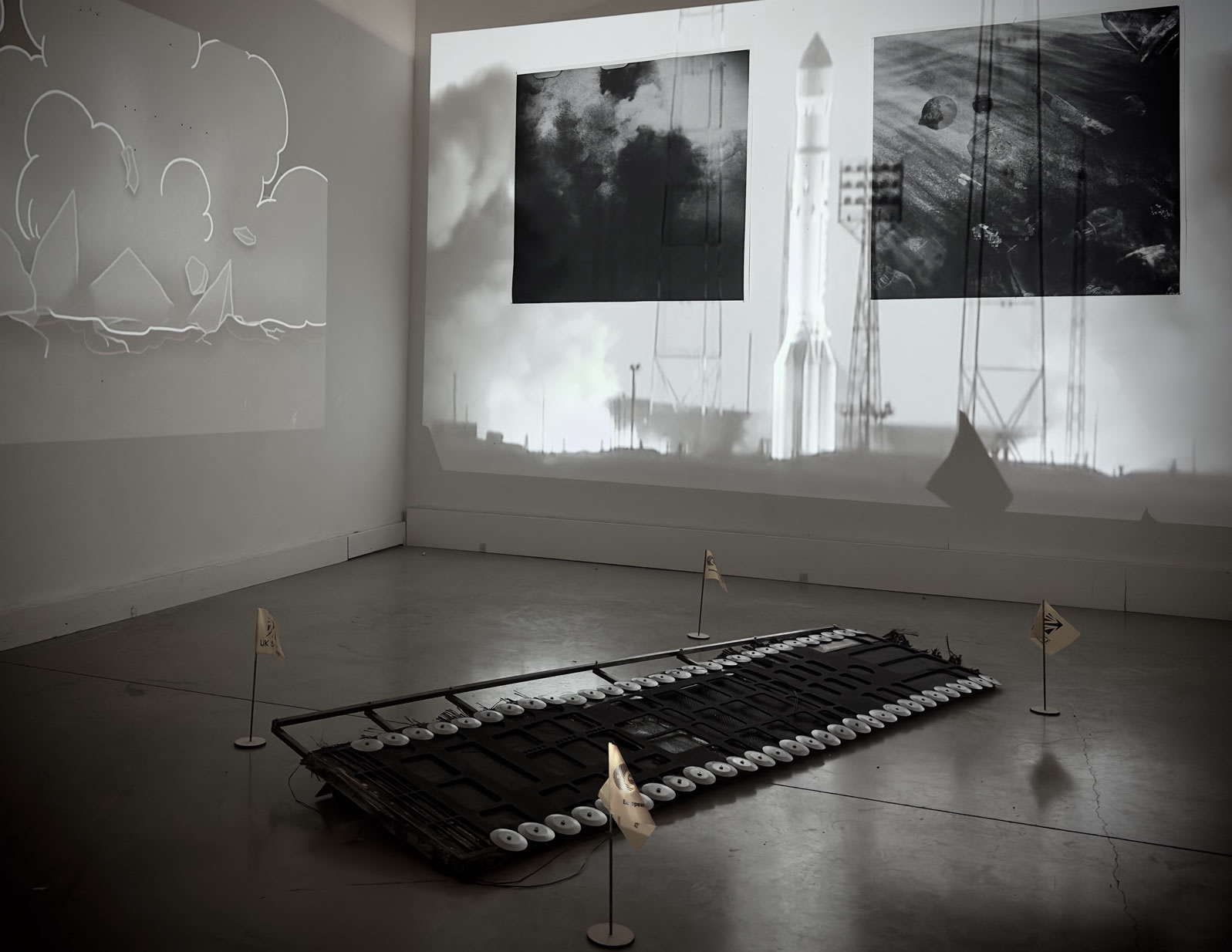 Installation featuring  sculpture, location flags, film still of rocket launch, an animated explosion and two photographs.