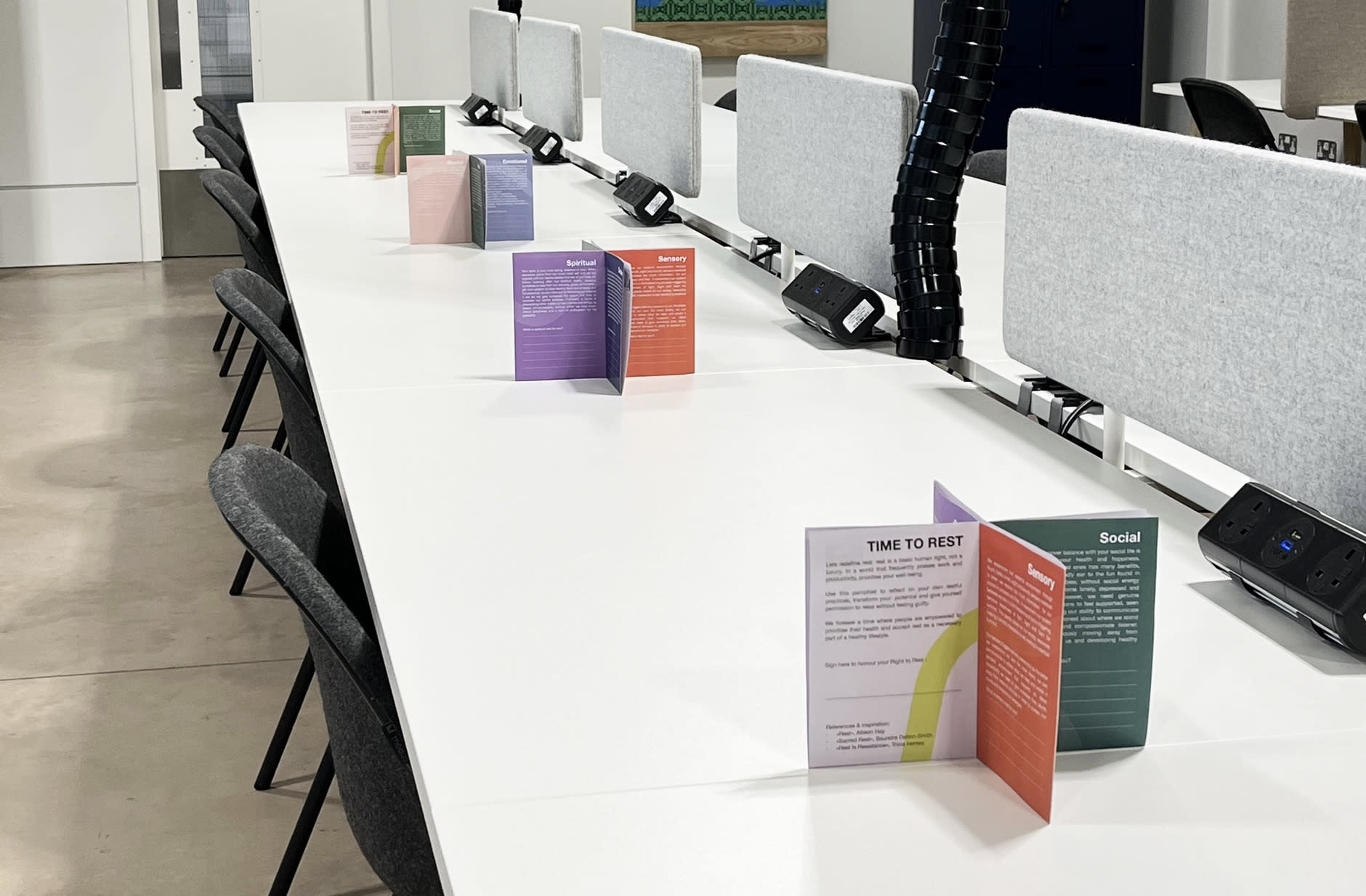 The image shows four pamphlets placed on tables at the RCA Battersea, quiet space campus, showing how they can be presented.