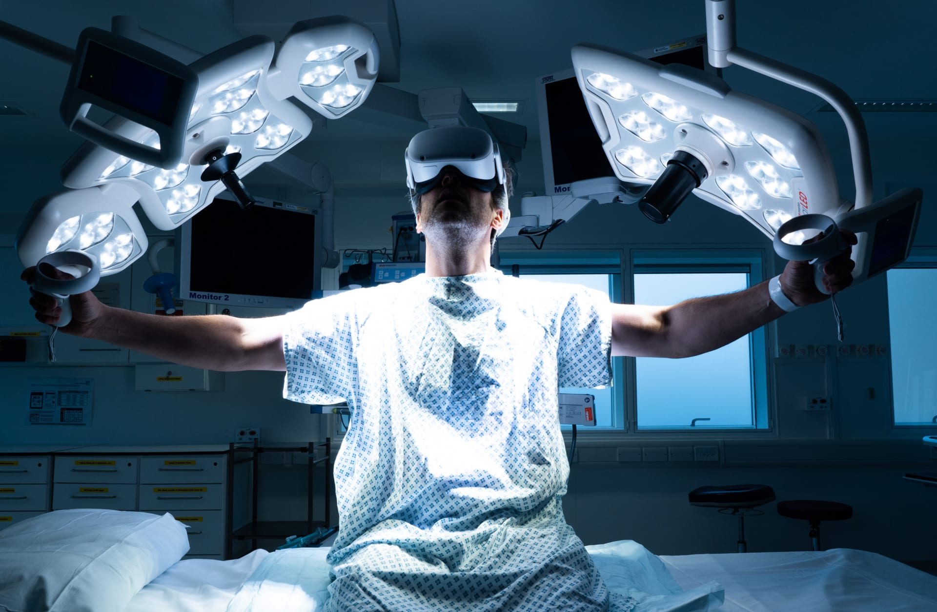 A photograph of Justin Piccirilli dressed in a hospital gown, wearing a VR headset and sitting on an operating theatre table. 