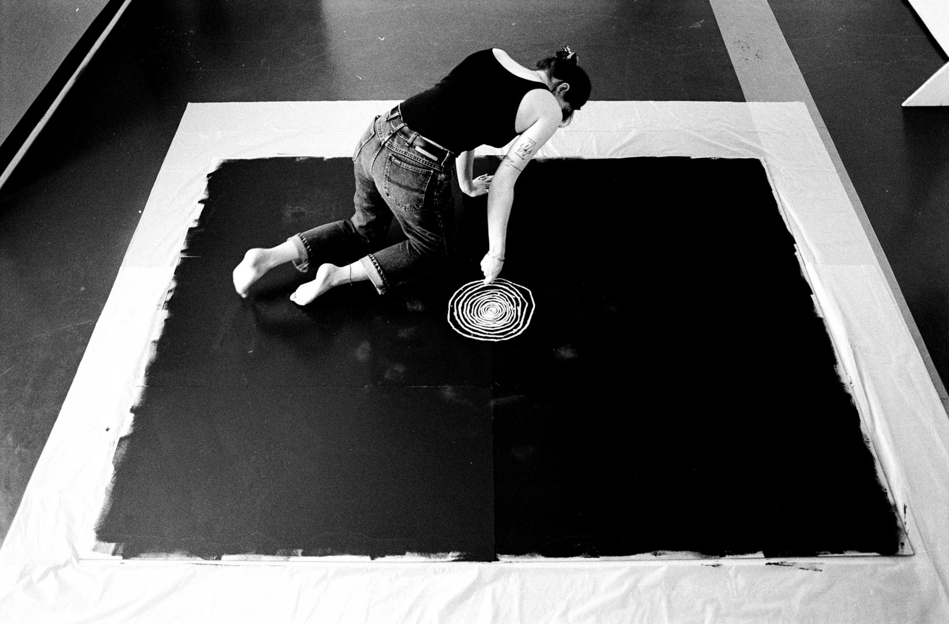 black and white image of the artist, taken from above, shows the artist drawing circles that get progressively bigger 