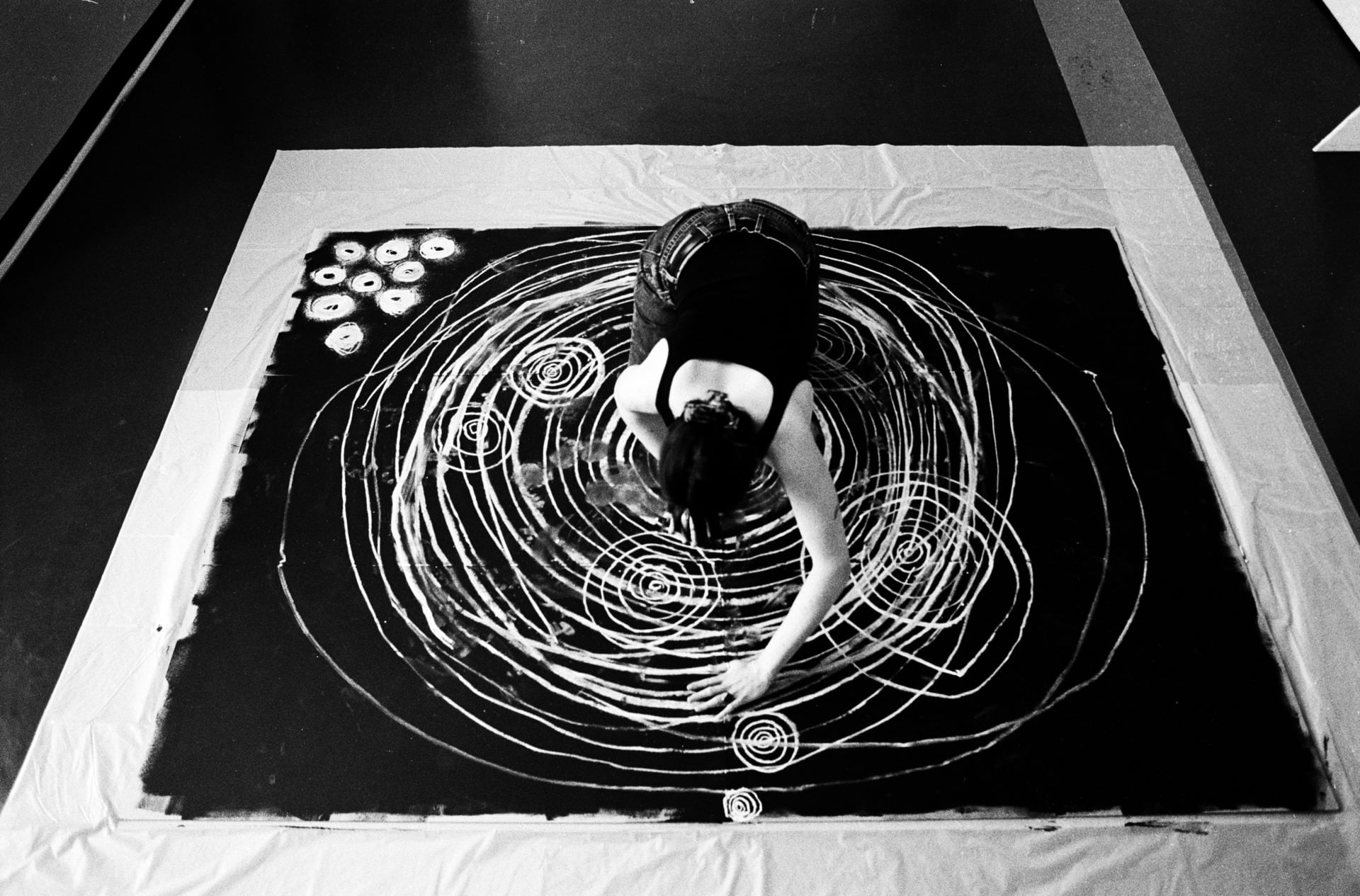 black and white image of the artist, taken from above, shows the artist drawing circles that get progressively bigger 