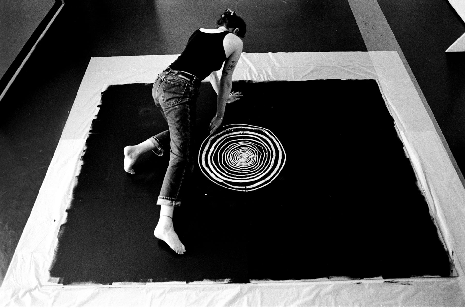 black and white image of the artist, taken from above, shows the artist drawing circles that get progressively bigger 