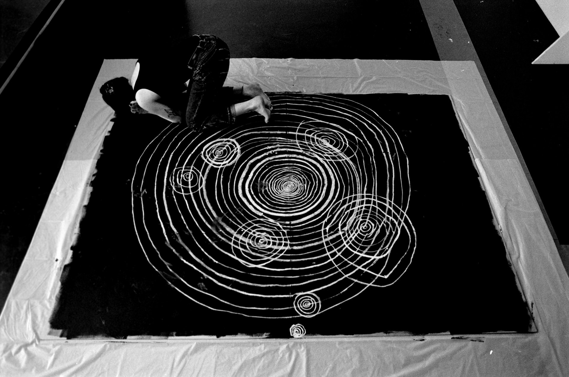 black and white image of the artist, taken from above, shows the artist drawing circles that get progressively bigger 