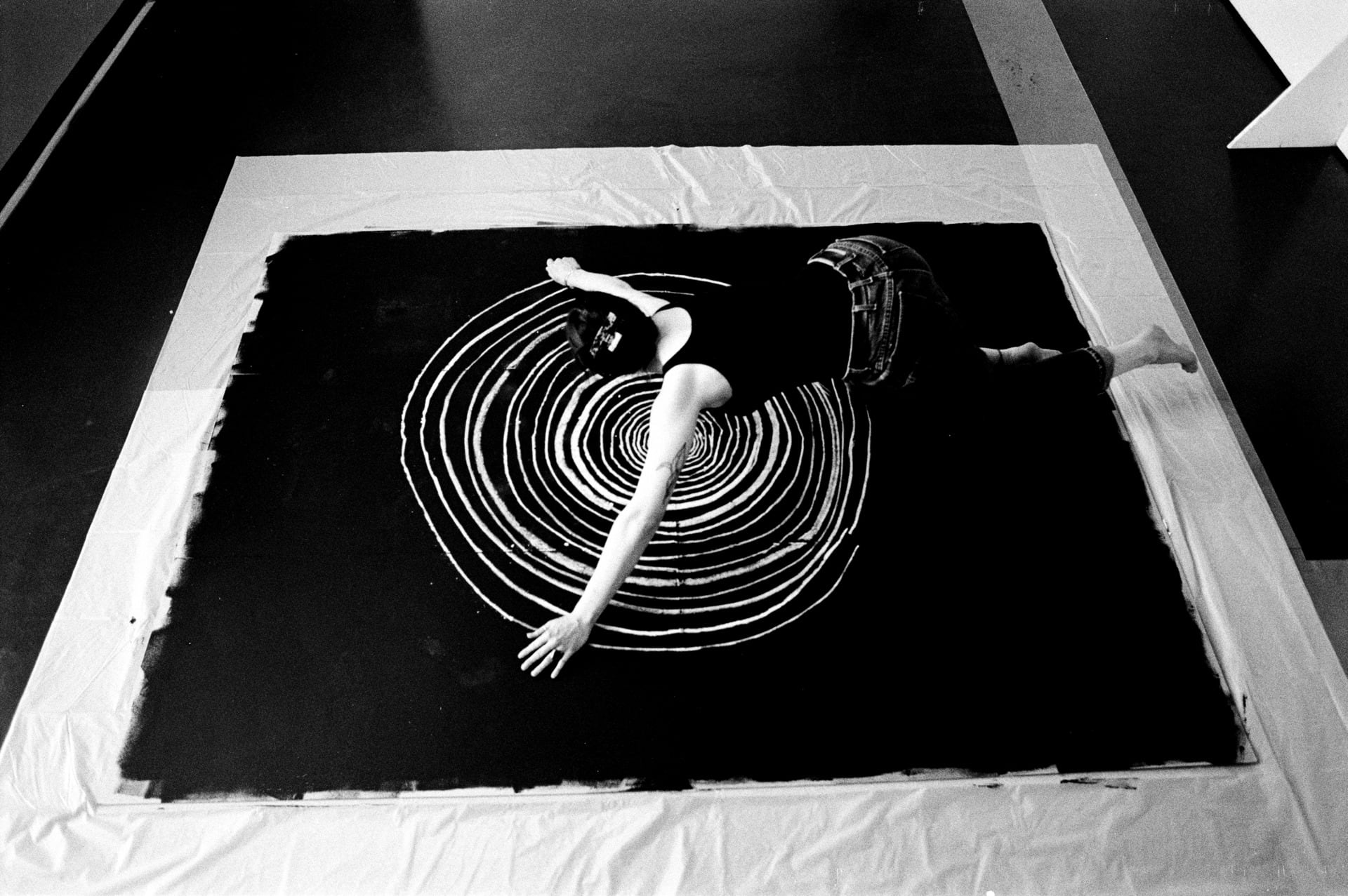 black and white image of the artist, taken from above, shows the artist drawing circles that get progressively bigger 