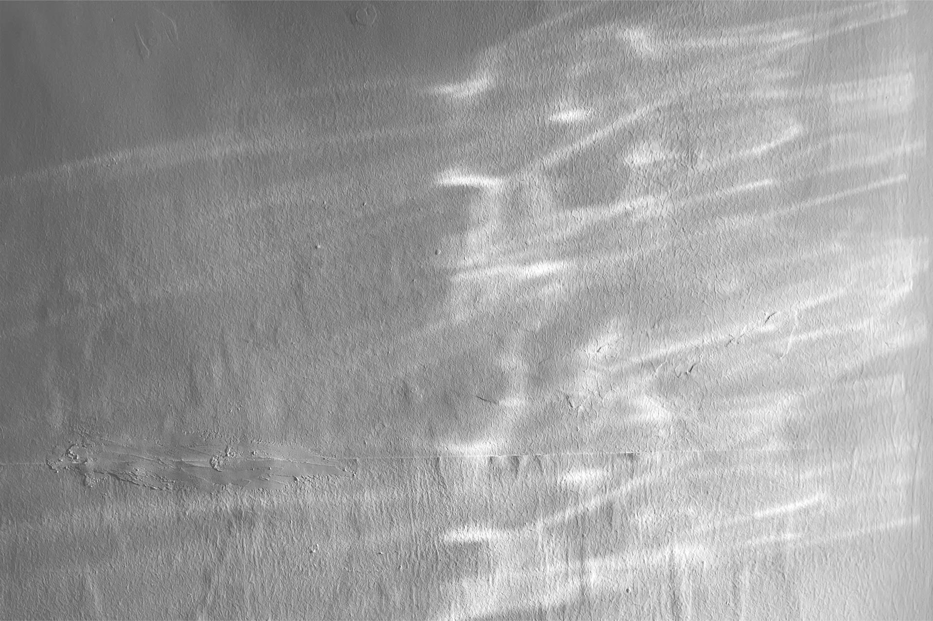 Black and white photograph of wavy light patters on a white wall 