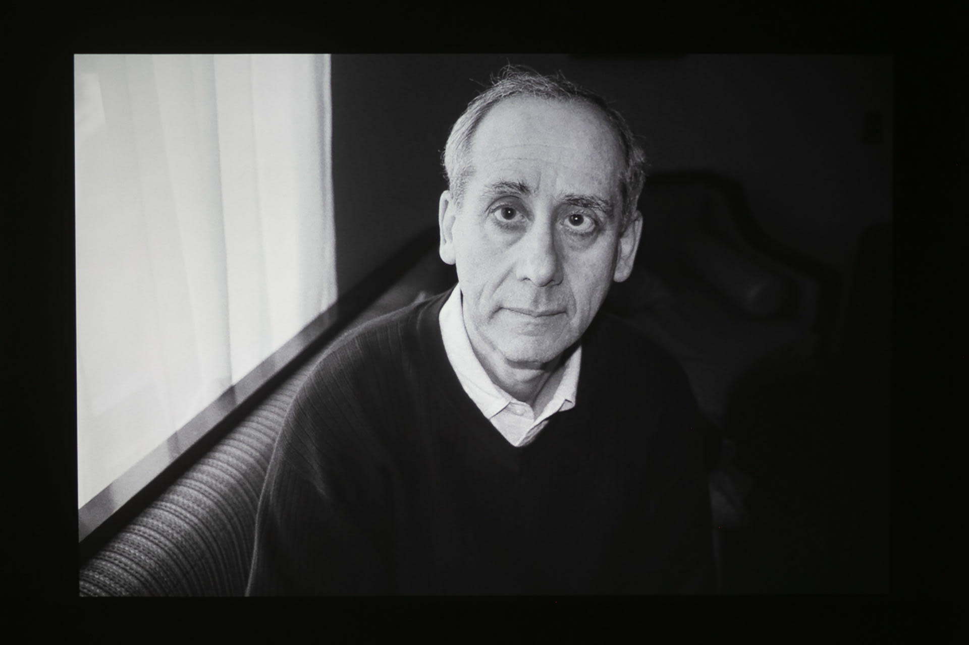Man looking at camera with his face lit by a window next to him. Black and white.