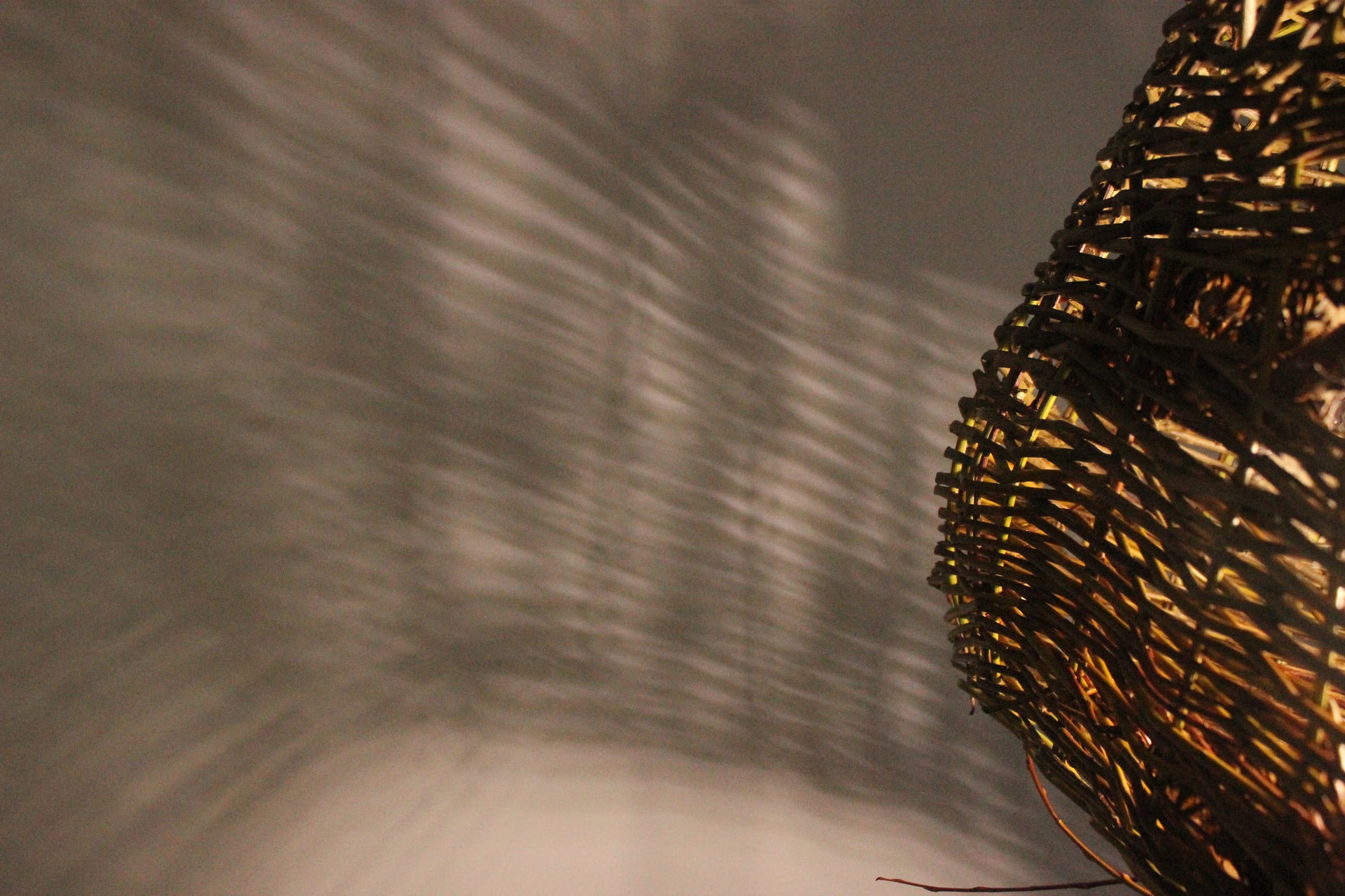 Willow woven lampshade lit from within throwing irregular shadows on wall behind with a whiter light