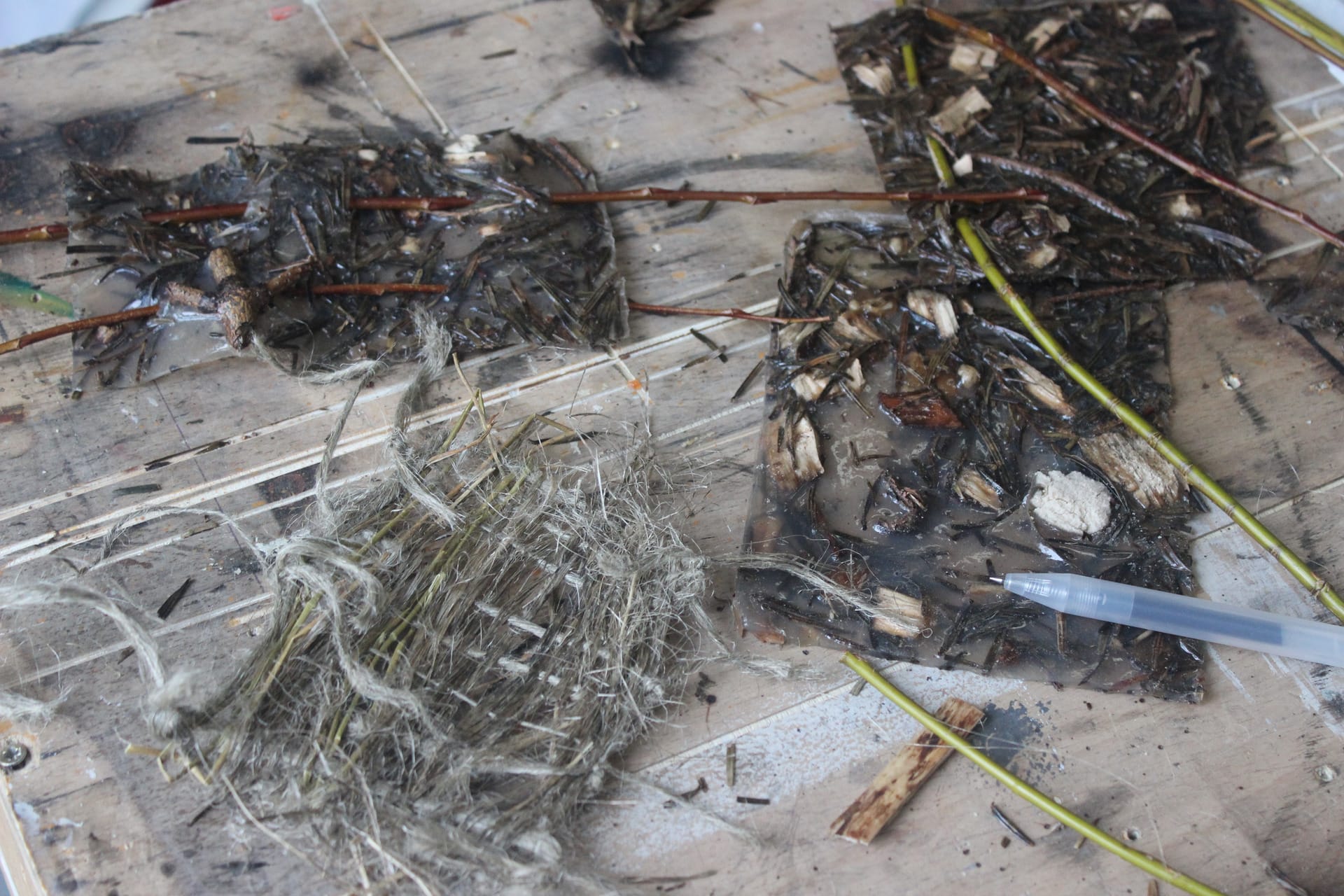 A collection of bio plastics and woven flax pieces on a studio work bench with strands of willow embedded into some plastics