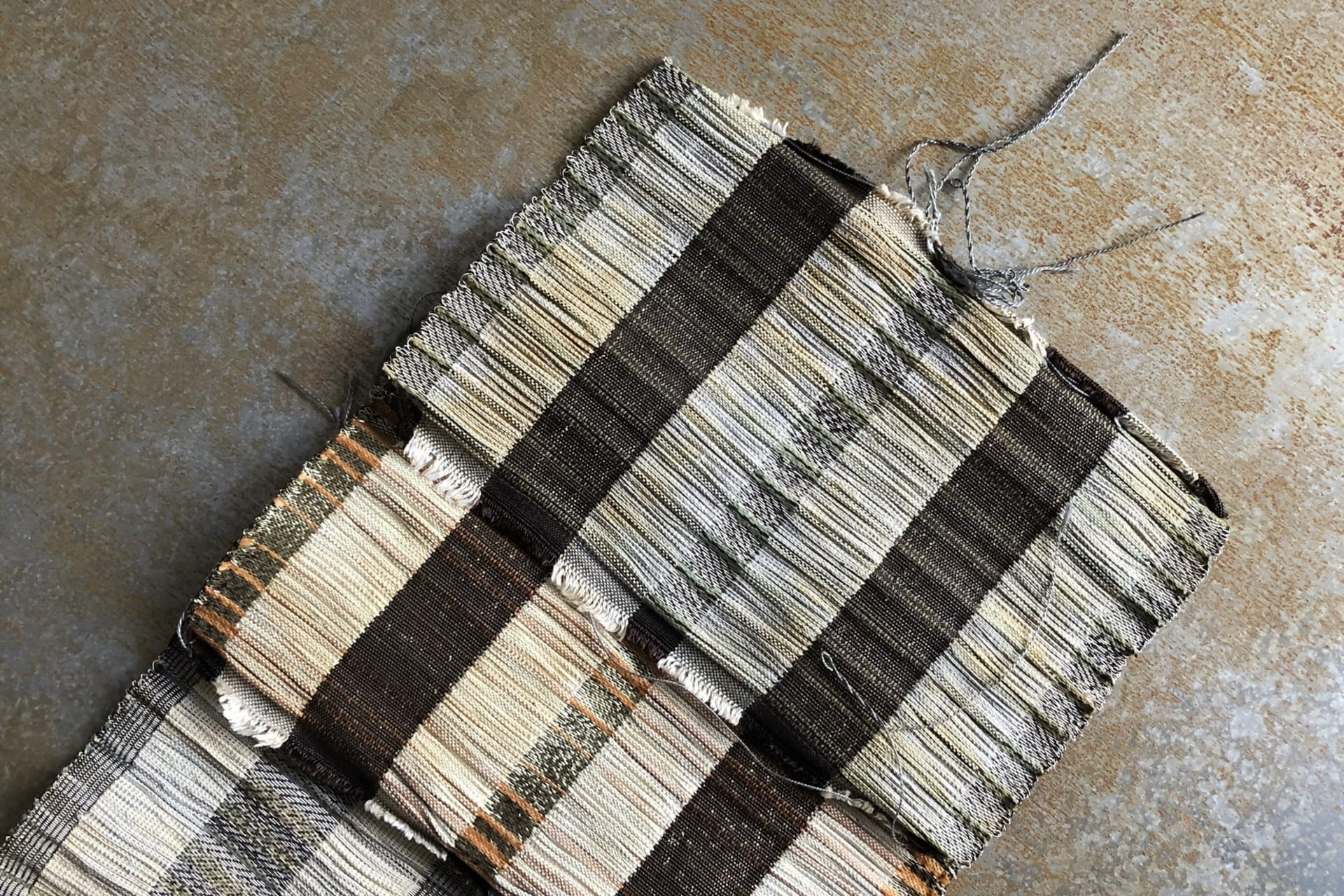 Three woven samples, layered on top of one another. Rusted metal background