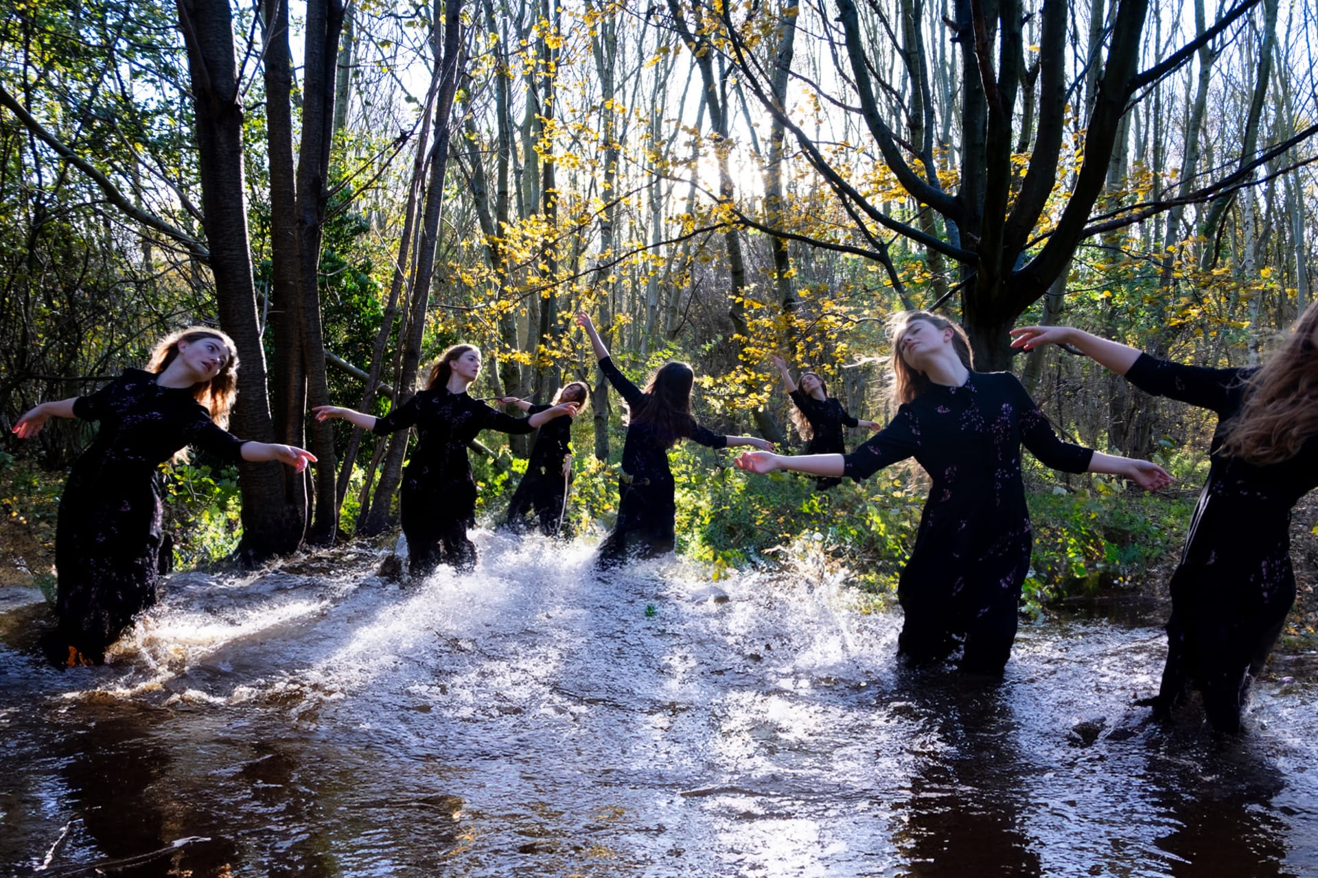 An image of 7 of the same woman dancing in a flood in the forest.