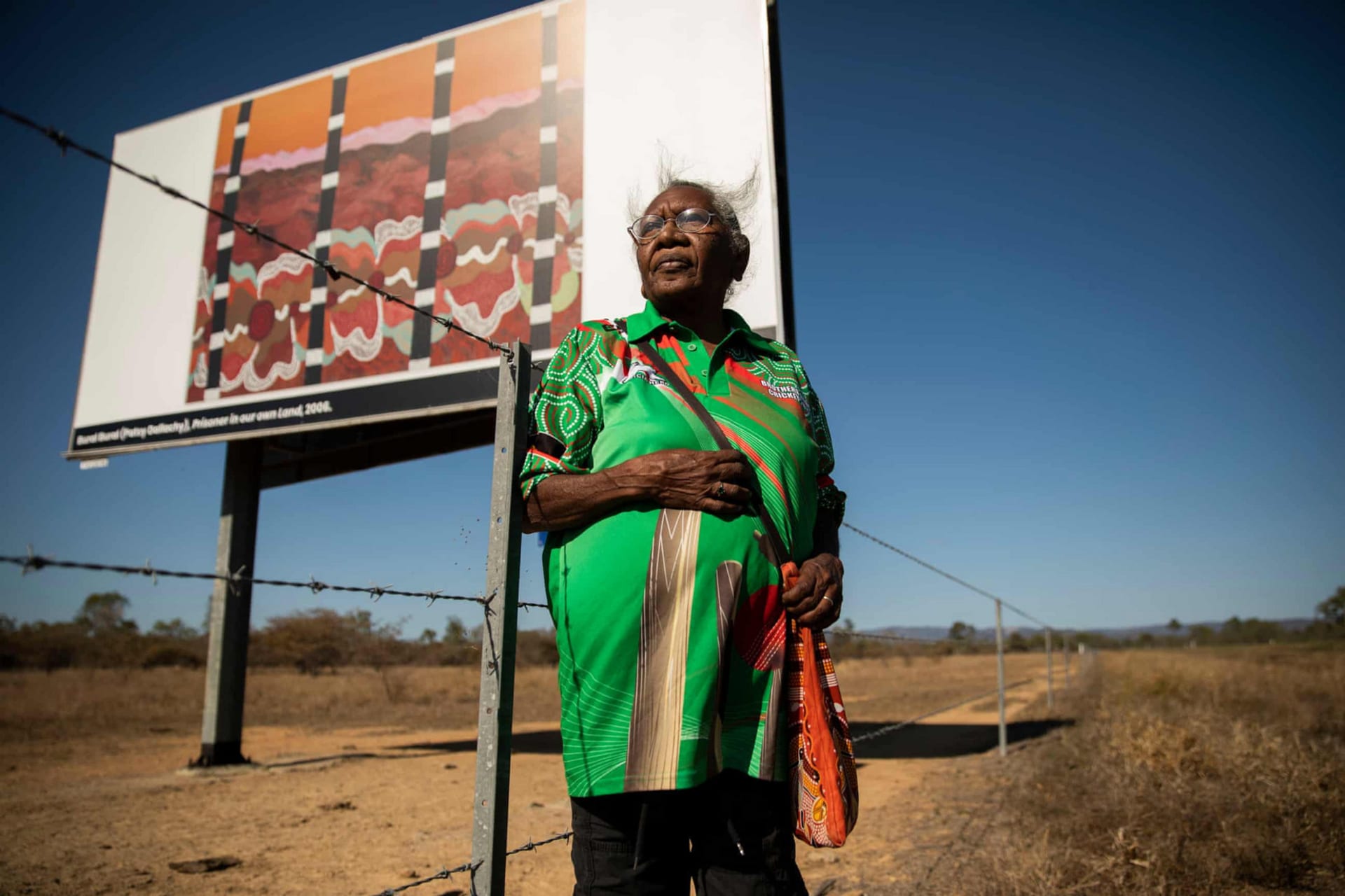 Bural Bural (Patsy Dallachy) in front of billboard artwork, Prisoner On Our Own Land, 2006. Image by Sean Davey, 2022.