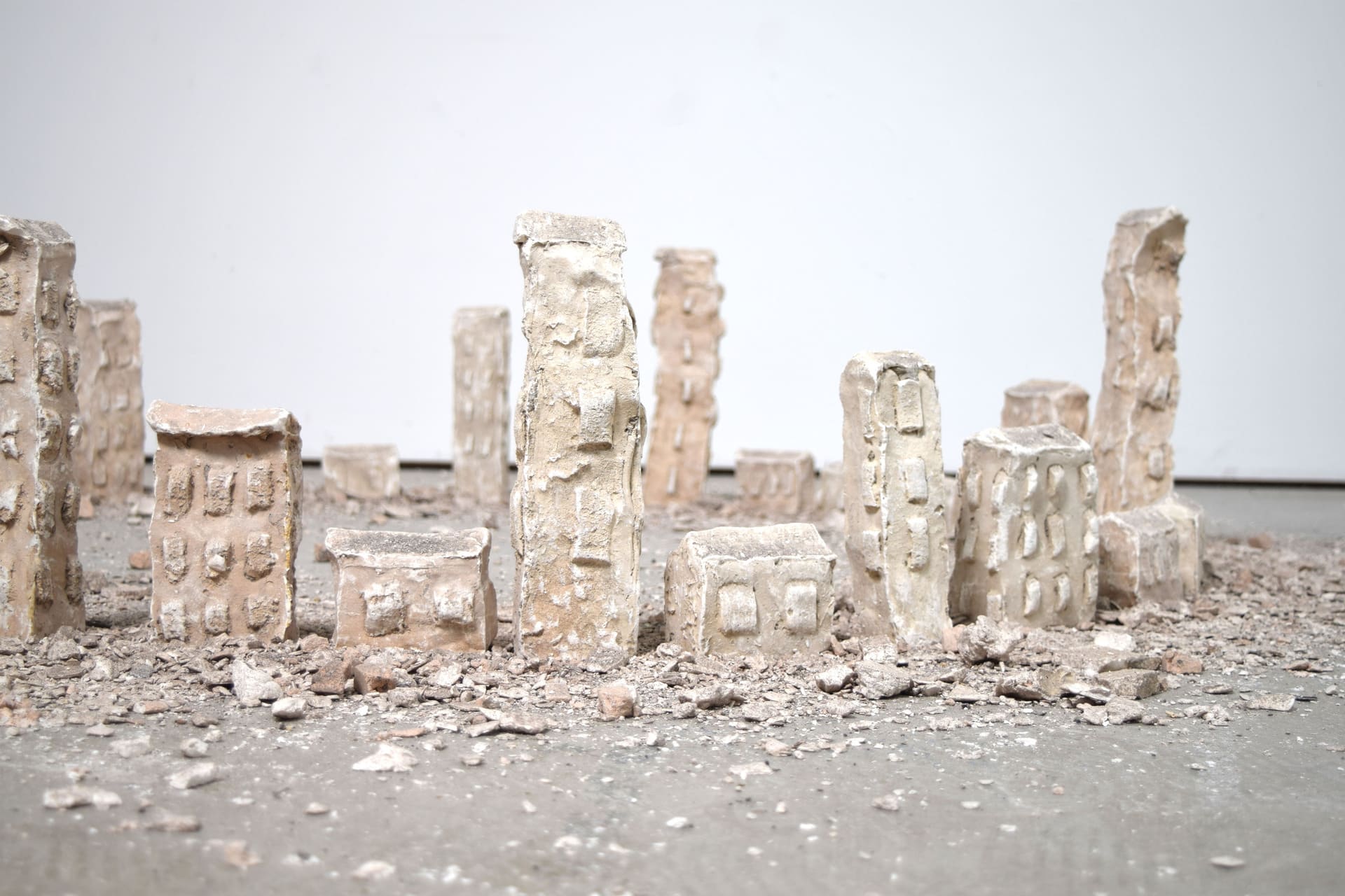 Thirty plaster towers ranging in height from 30-6cm, are positioned in a large circle on the floor with a halo of rubble.