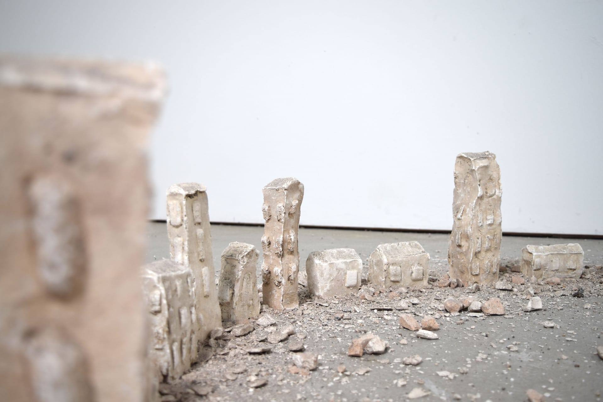 Thirty plaster towers ranging in height from 30-6cm, are positioned in a large circle on the floor with a halo of rubble.