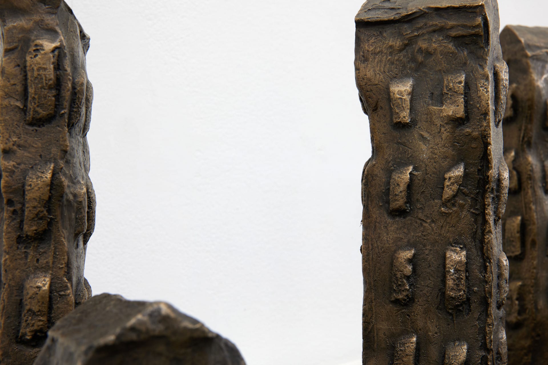 Seven Bronze disfigured towers standing side by side on a plinth.