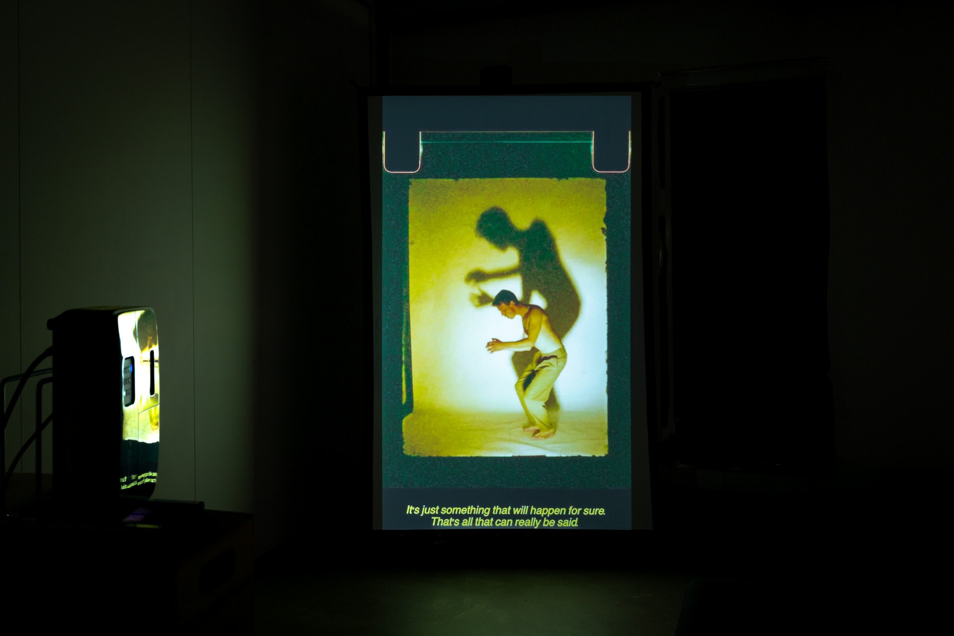 three figures watching a flickery video projection that shows a male figure dancing with a large shadow behind him