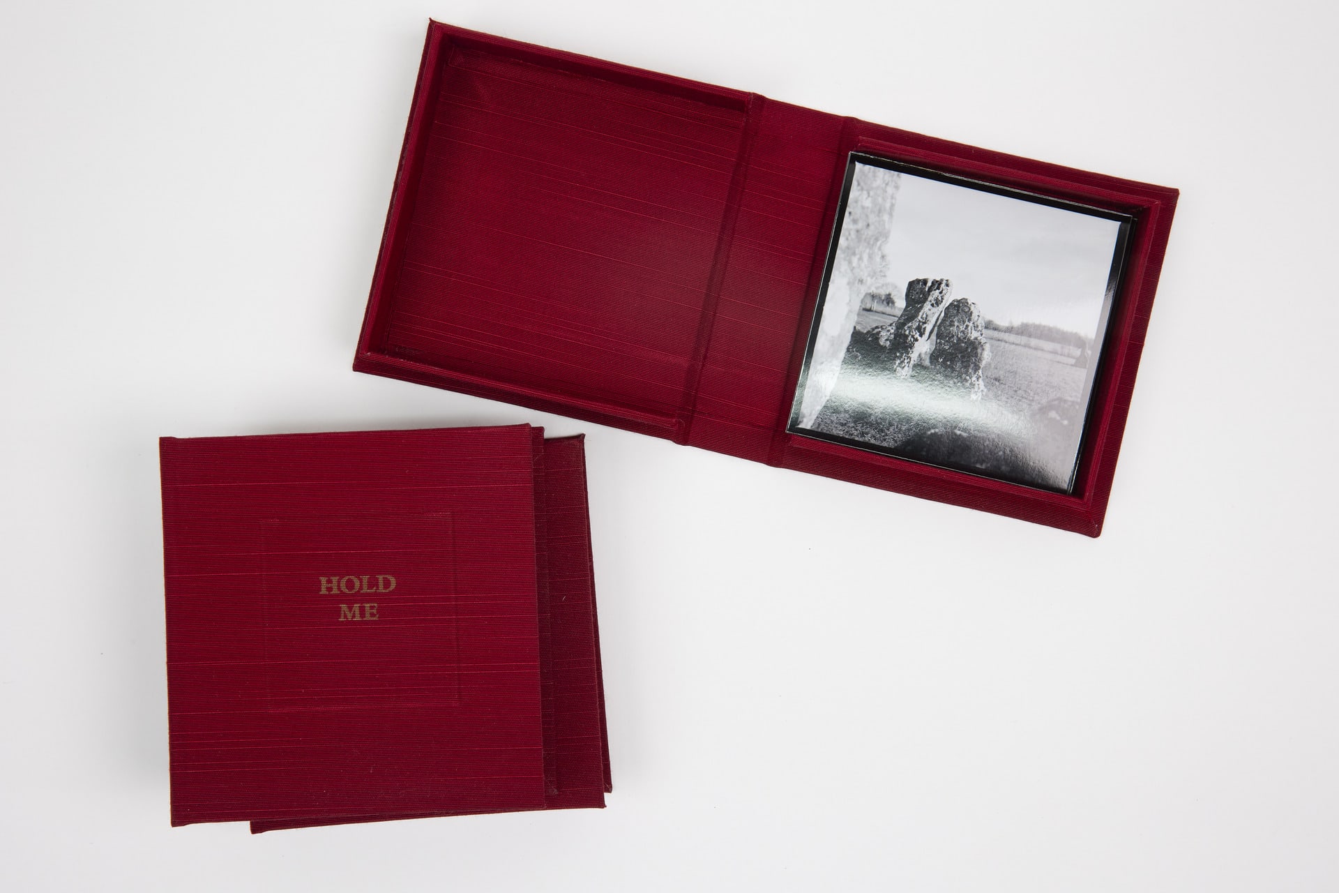 Small red boxes photographed from above. One red box lies open and inside is a black and white photograph of a stone.